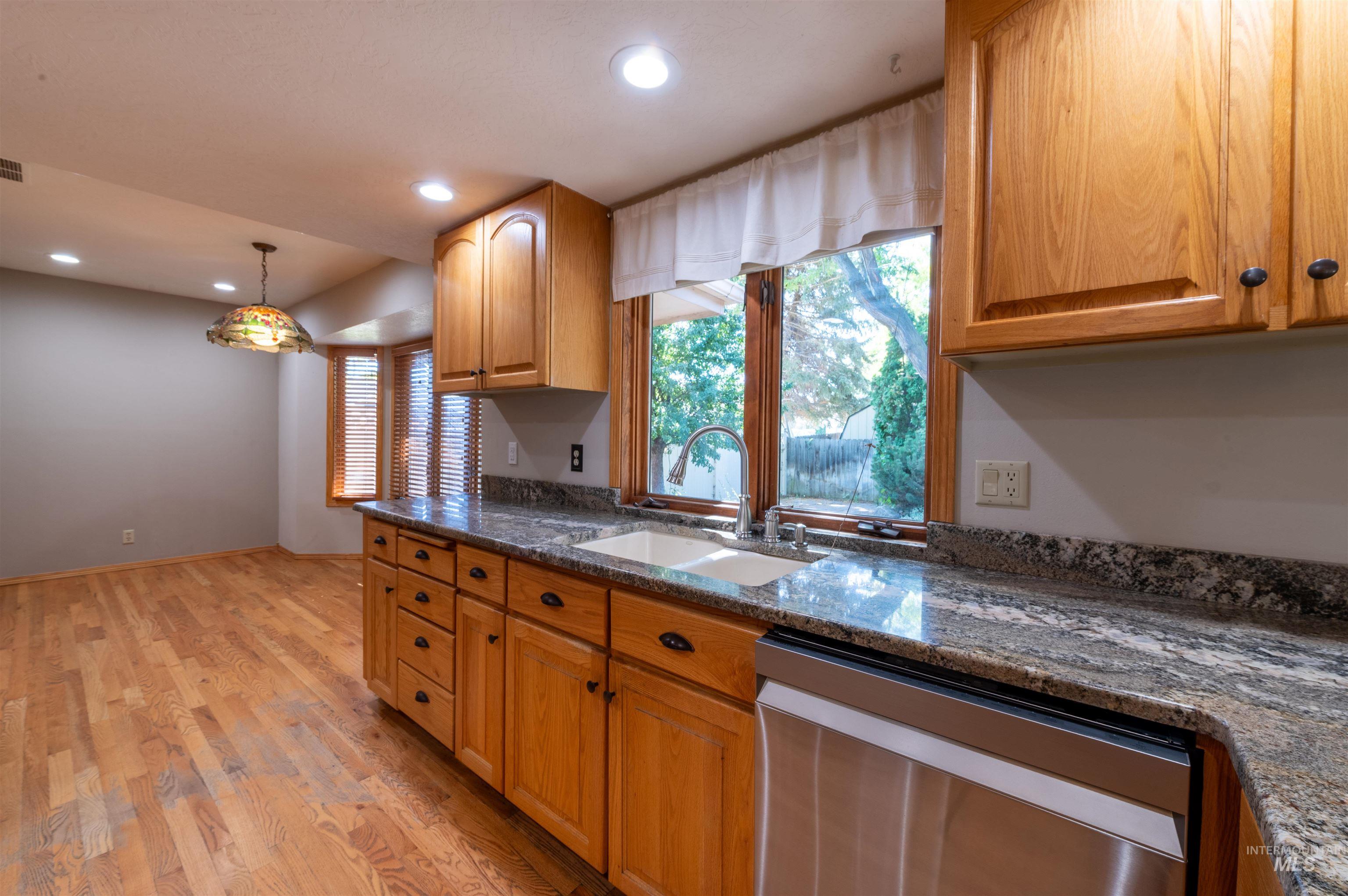 Kitchen with decorative light fixtures, stainless steel dishwasher, recessed lighting, light wood finished floors, and dark stone counters