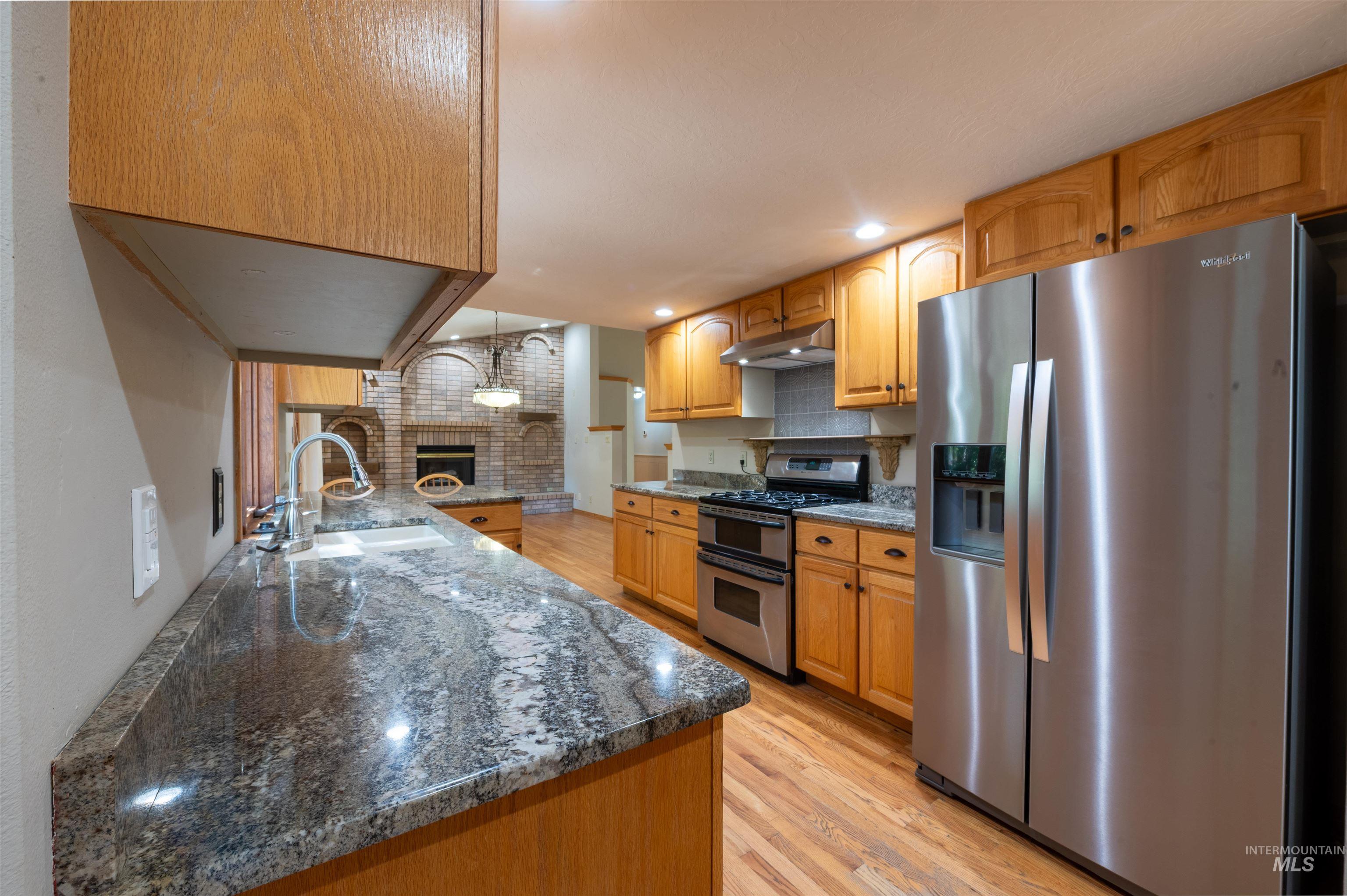 Kitchen featuring dark stone counters, light wood-type flooring, appliances with stainless steel finishes, decorative light fixtures, and recessed lighting