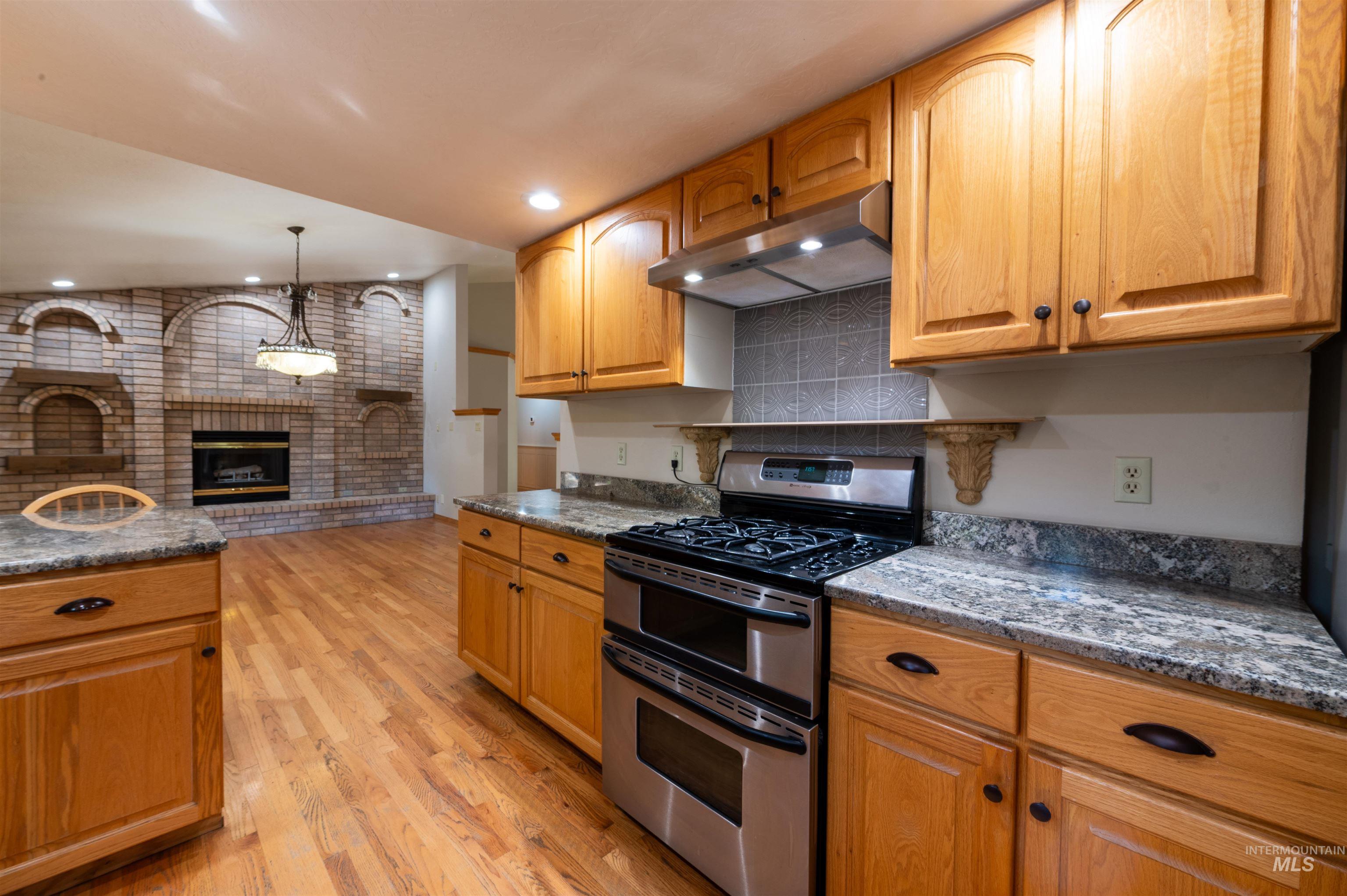 Kitchen featuring double oven range, under cabinet range hood, light wood finished floors, pendant lighting, and brown cabinetry