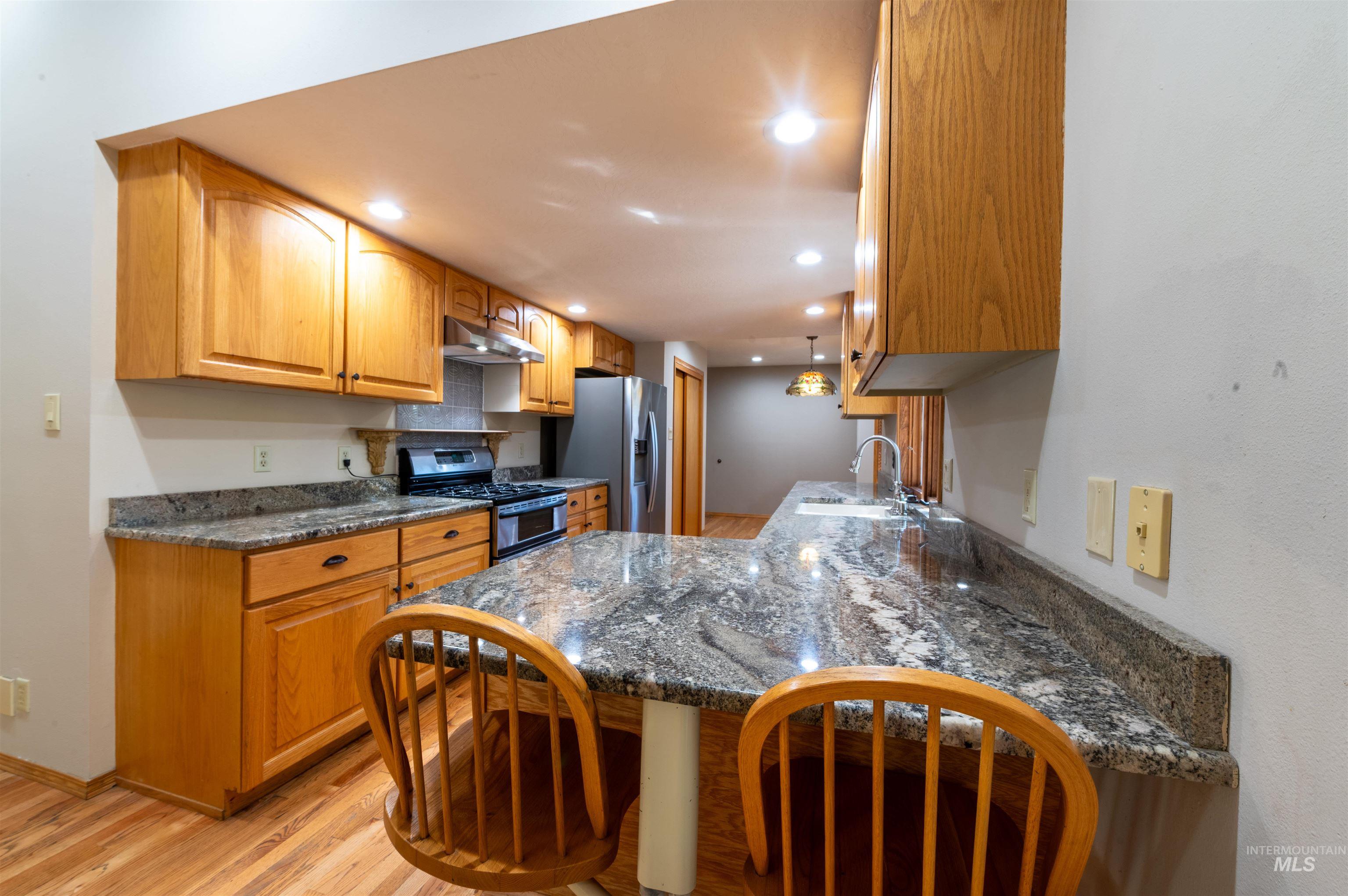 Kitchen featuring dark stone countertops, light wood-style flooring, stainless steel appliances, pendant lighting, and recessed lighting