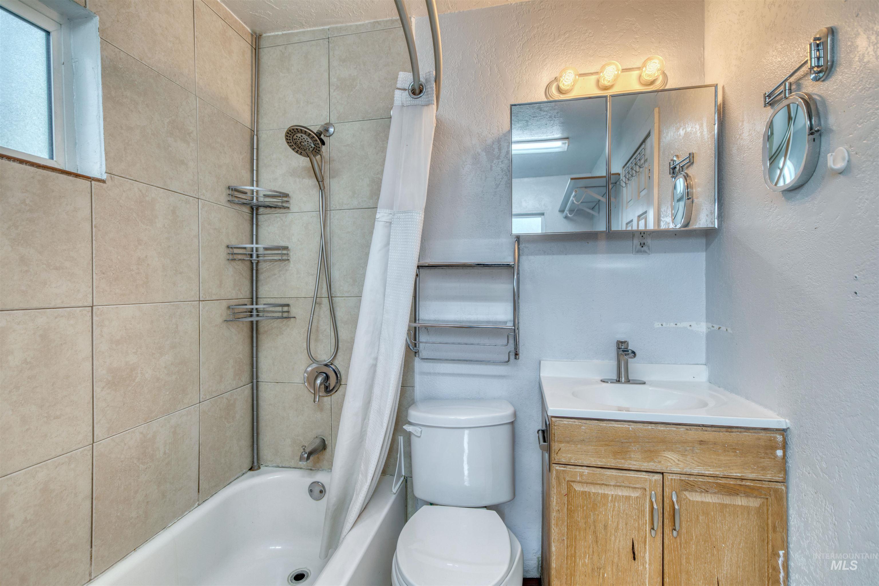 Bathroom featuring a textured wall, shower / bath combo with shower curtain, and vanity