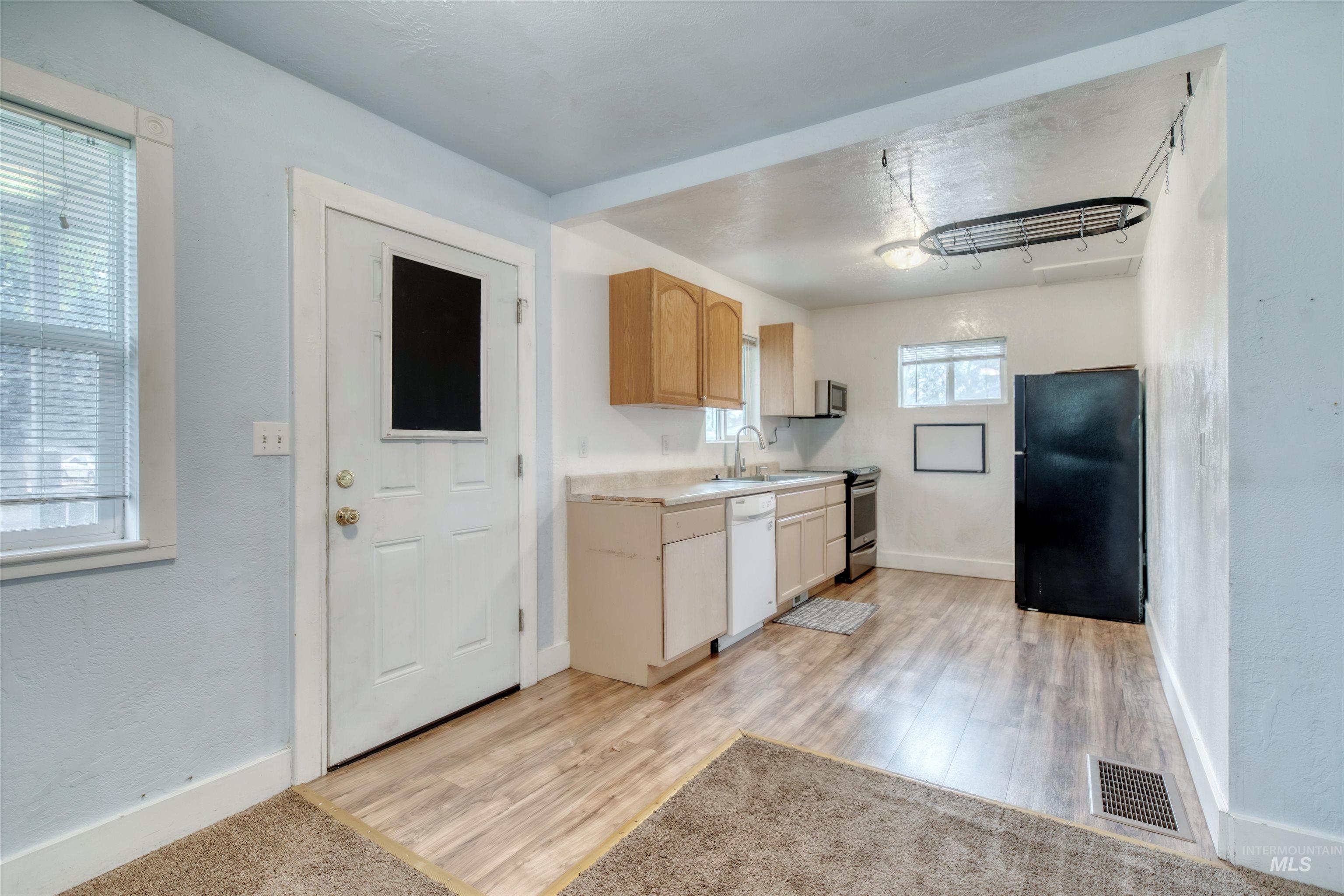 Kitchen featuring light countertops, freestanding refrigerator, light brown cabinetry, light wood-type flooring, and white dishwasher