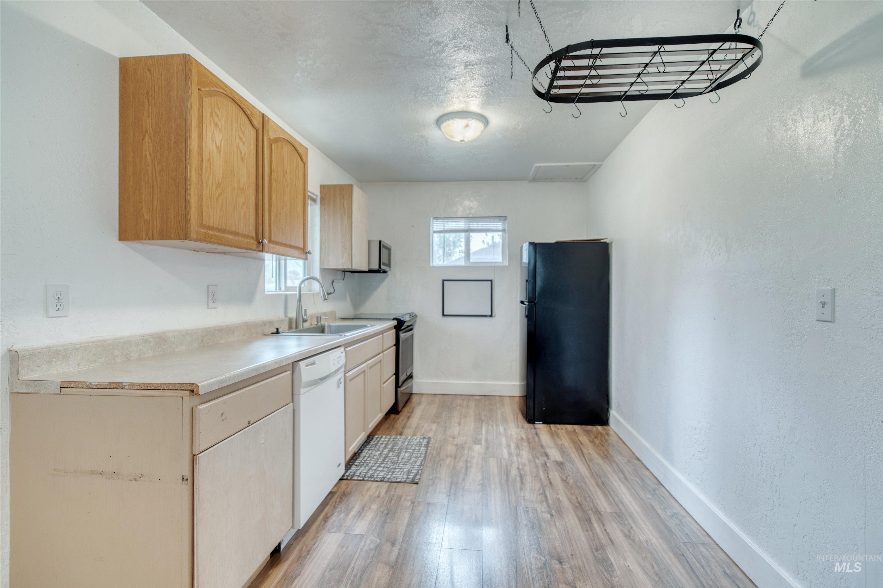Kitchen featuring light countertops, appliances with stainless steel finishes, light brown cabinets, light wood-type flooring, and a textured ceiling