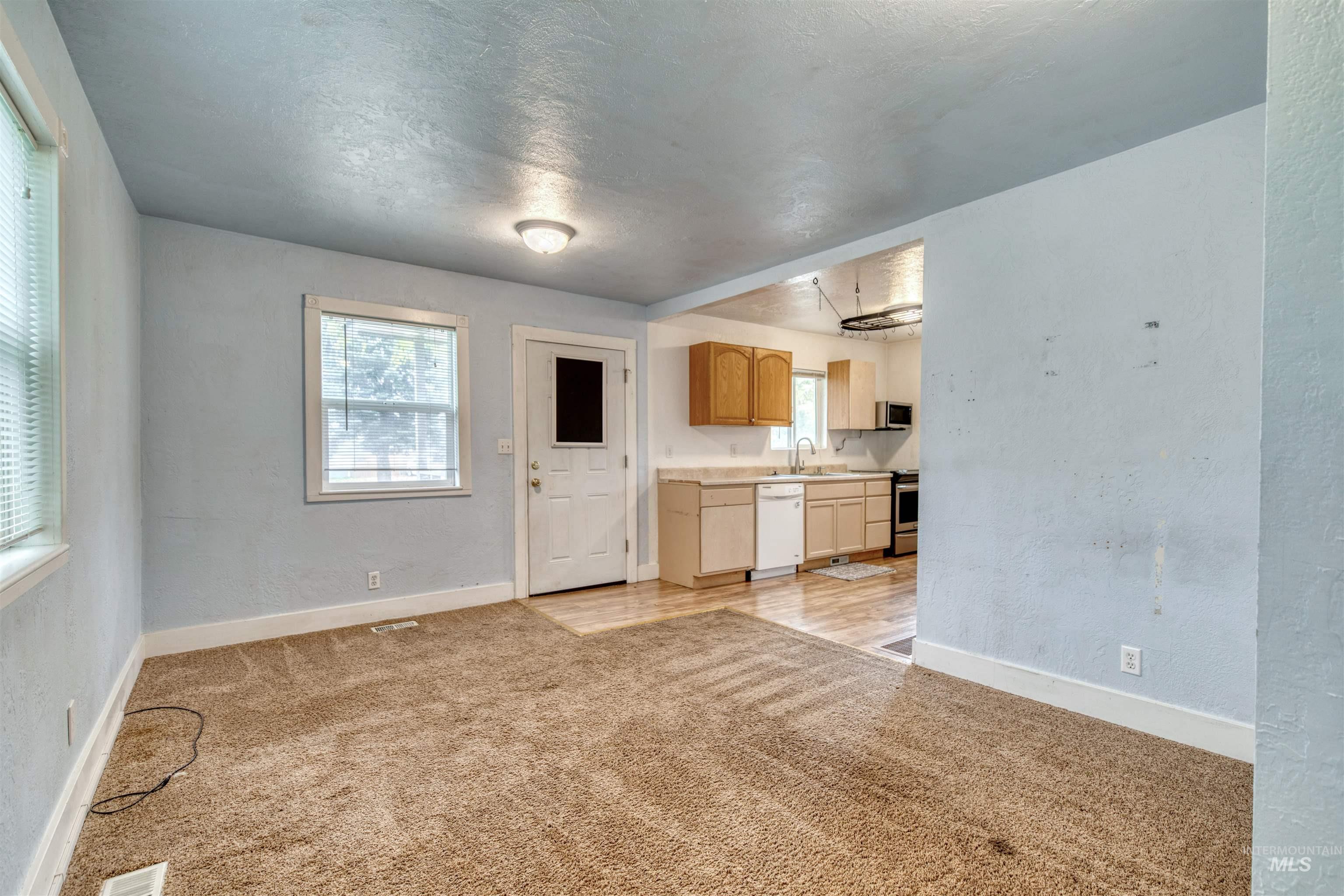 Kitchen with a textured wall, light colored carpet, light countertops, white dishwasher, and light brown cabinets