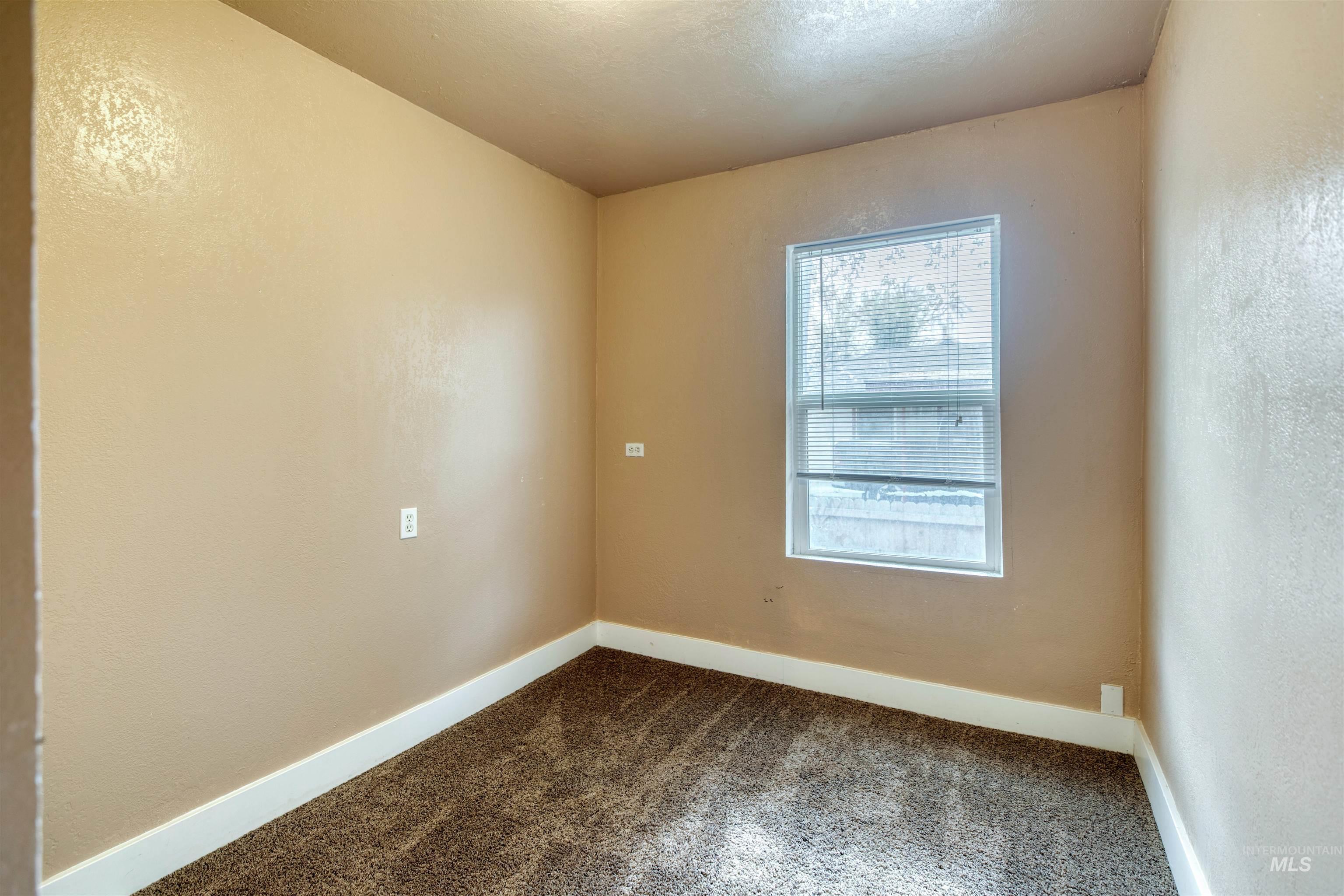 Unfurnished room featuring dark colored carpet and a textured wall