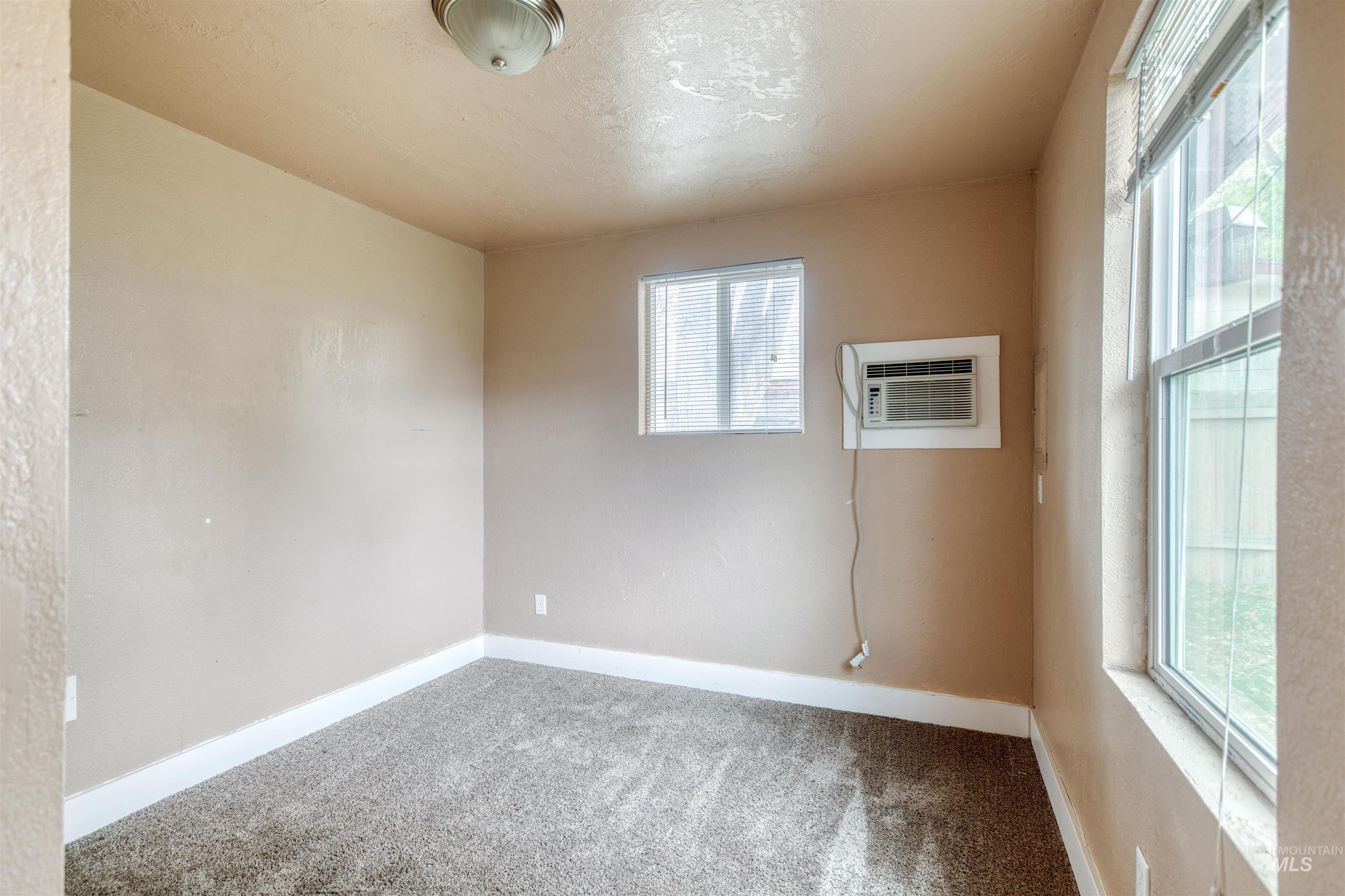 Carpeted empty room with a wall mounted AC and a textured ceiling