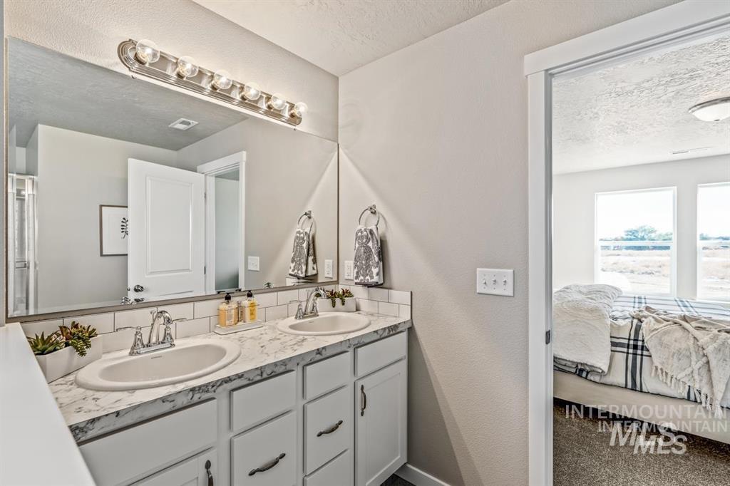 Ensuite bathroom featuring a textured ceiling, double vanity, and a textured wall
