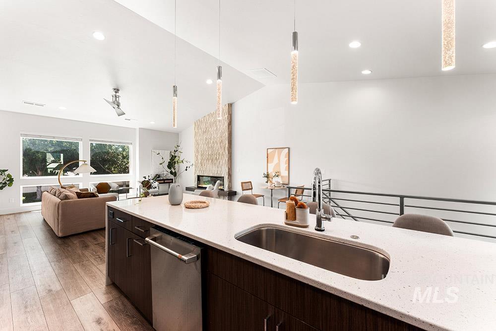 Kitchen with pendant lighting, light stone countertops, dark brown cabinets, stainless steel dishwasher, and open floor plan