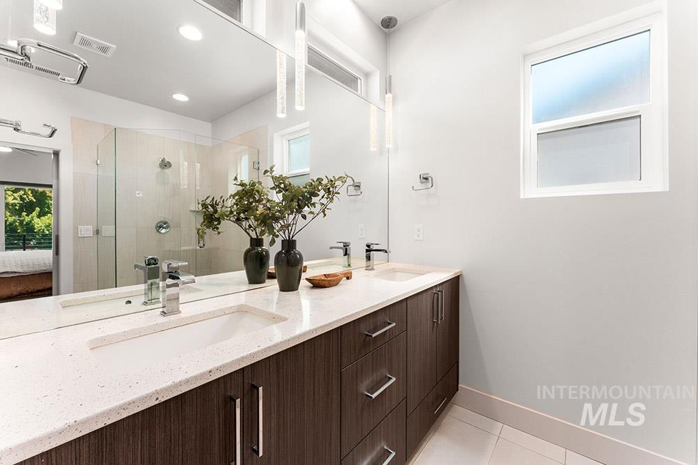 Ensuite bathroom featuring healthy amount of natural light, a stall shower, double vanity, light tile patterned floors, and recessed lighting