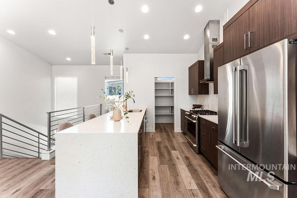 Kitchen featuring stainless steel appliances, dark brown cabinets, hanging light fixtures, dark wood-style floors, and light stone countertops