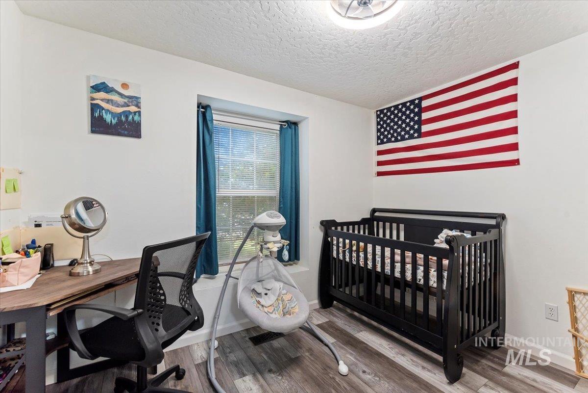 Bedroom featuring wood finished floors, a nursery area, a textured ceiling, and an office area