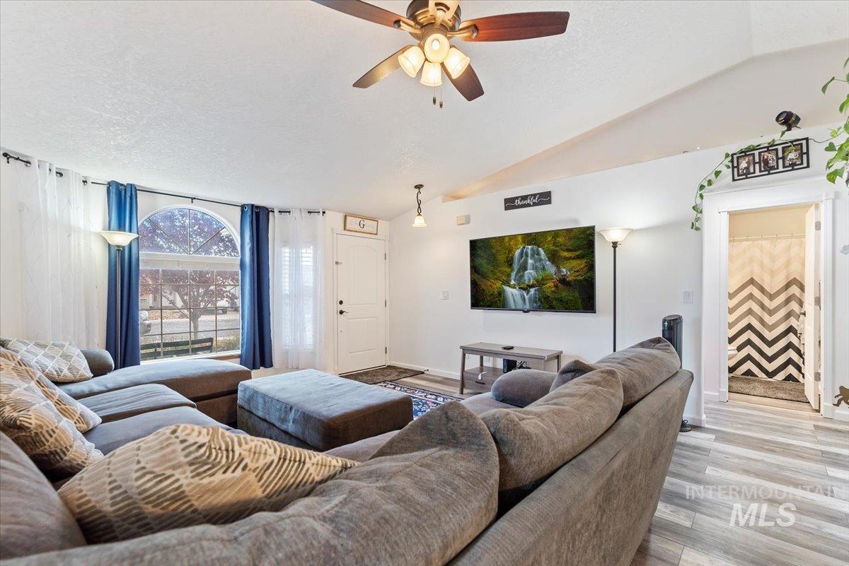Living room with wood finished floors, lofted ceiling, a ceiling fan, and a textured ceiling