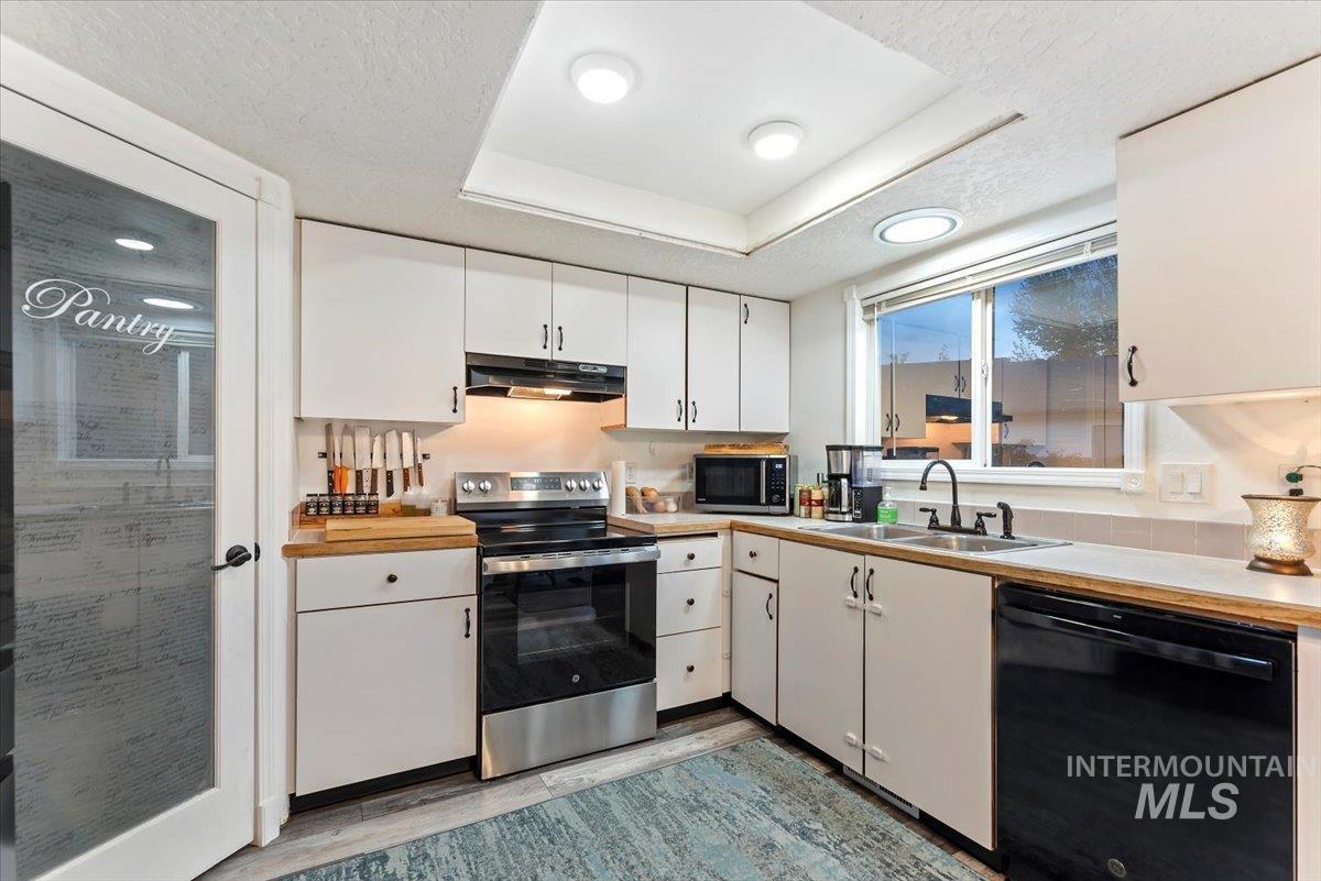 Kitchen with white cabinets, black appliances, light countertops, a raised ceiling, and a textured ceiling