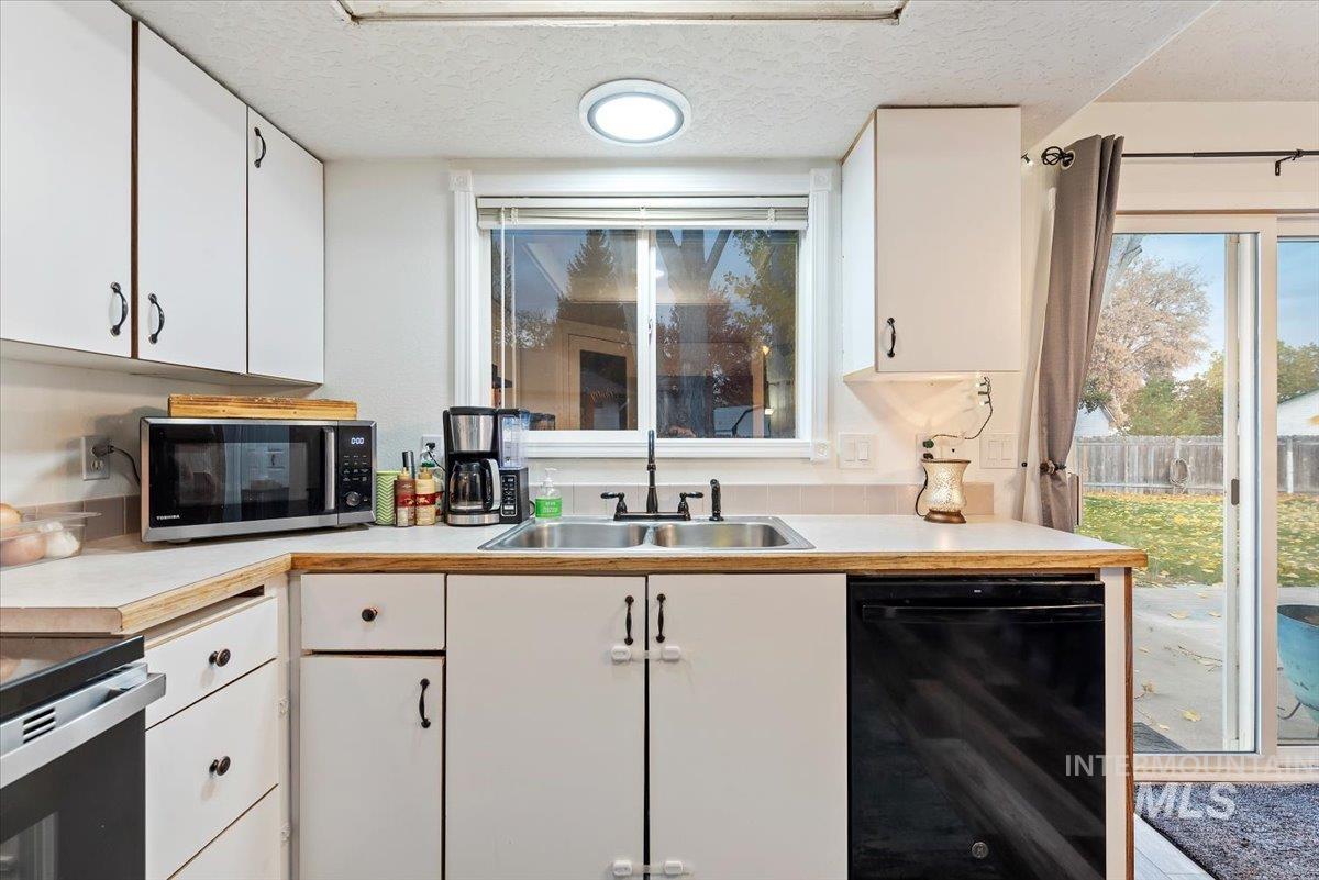 Kitchen with white cabinetry, light countertops, black dishwasher, a textured ceiling, and stainless steel microwave