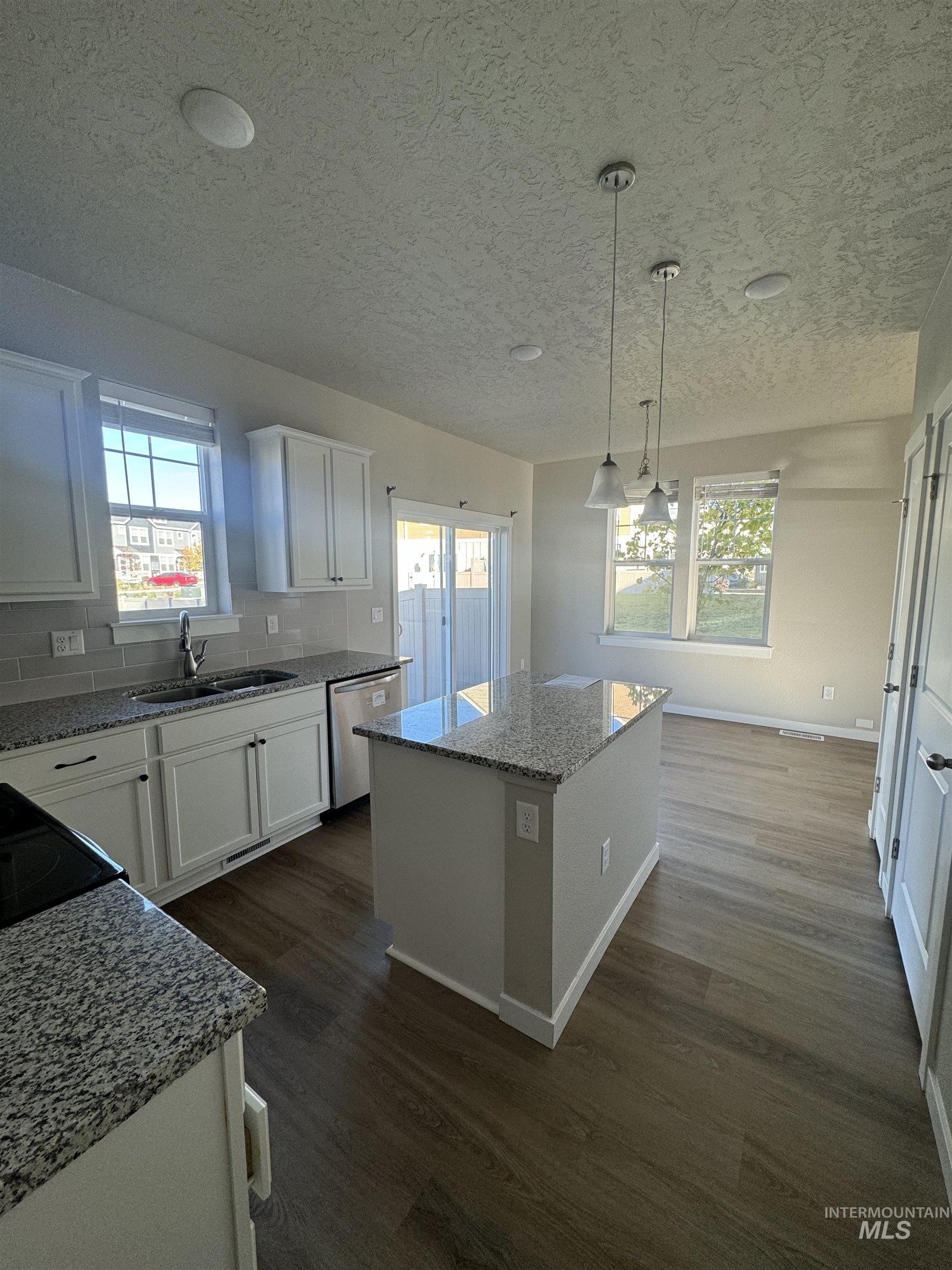 Kitchen featuring light stone counters, white cabinets, dark wood-style floors, a kitchen island, and pendant lighting