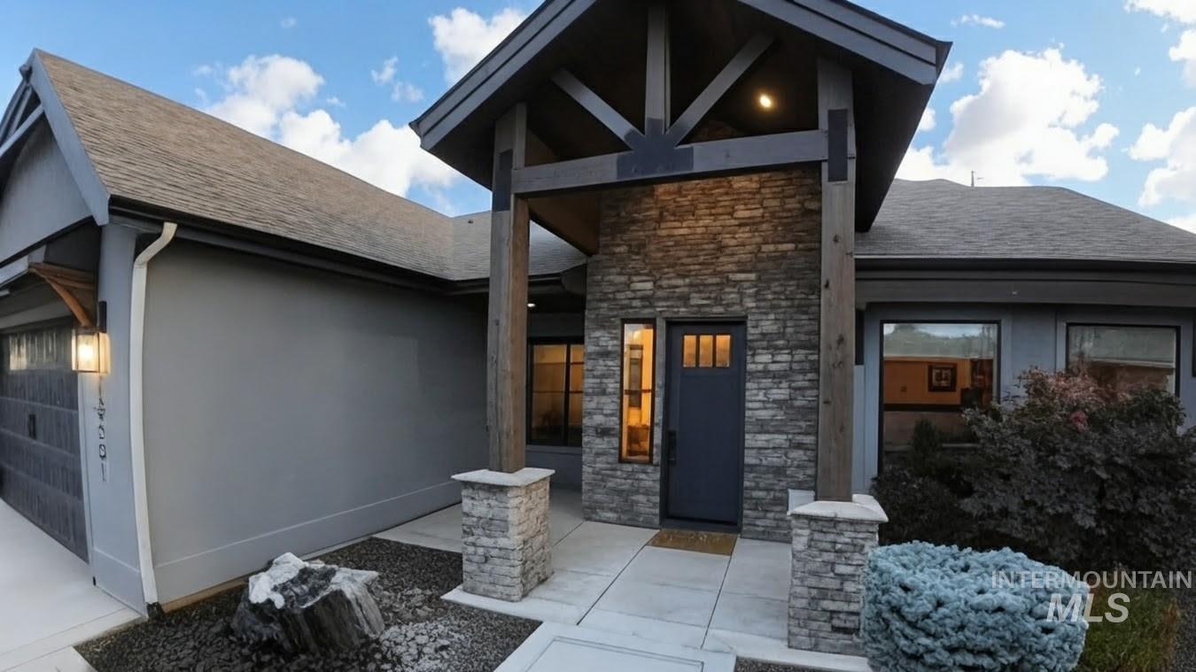 Doorway to property with stone siding, roof with shingles, an attached garage, and stucco siding