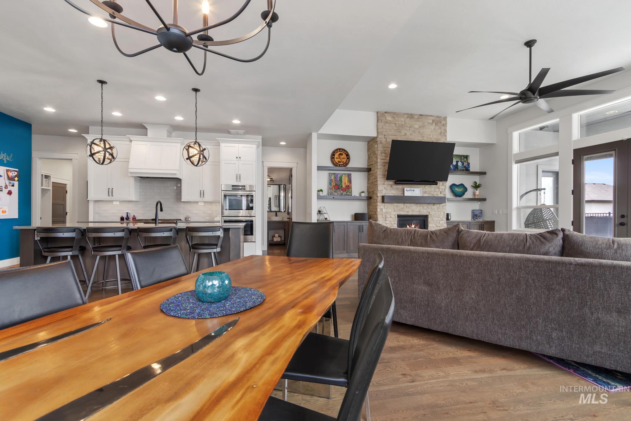 Dining space featuring dark wood-type flooring, a stone fireplace, a chandelier, a ceiling fan, and recessed lighting