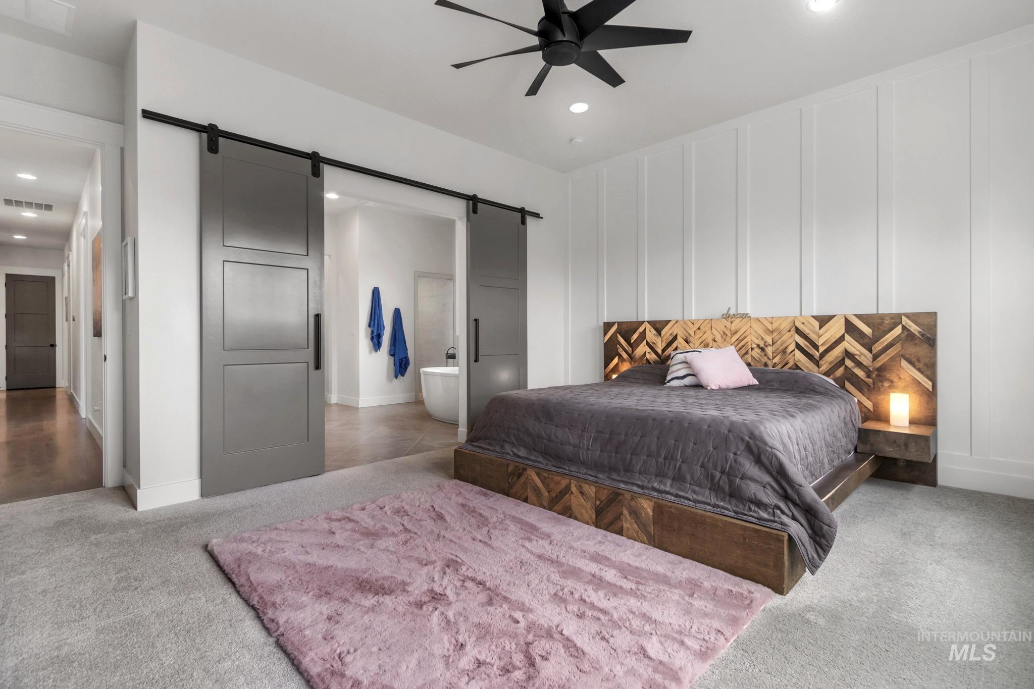 Bedroom with a decorative wall, a barn door, ensuite bathroom, light colored carpet, and recessed lighting