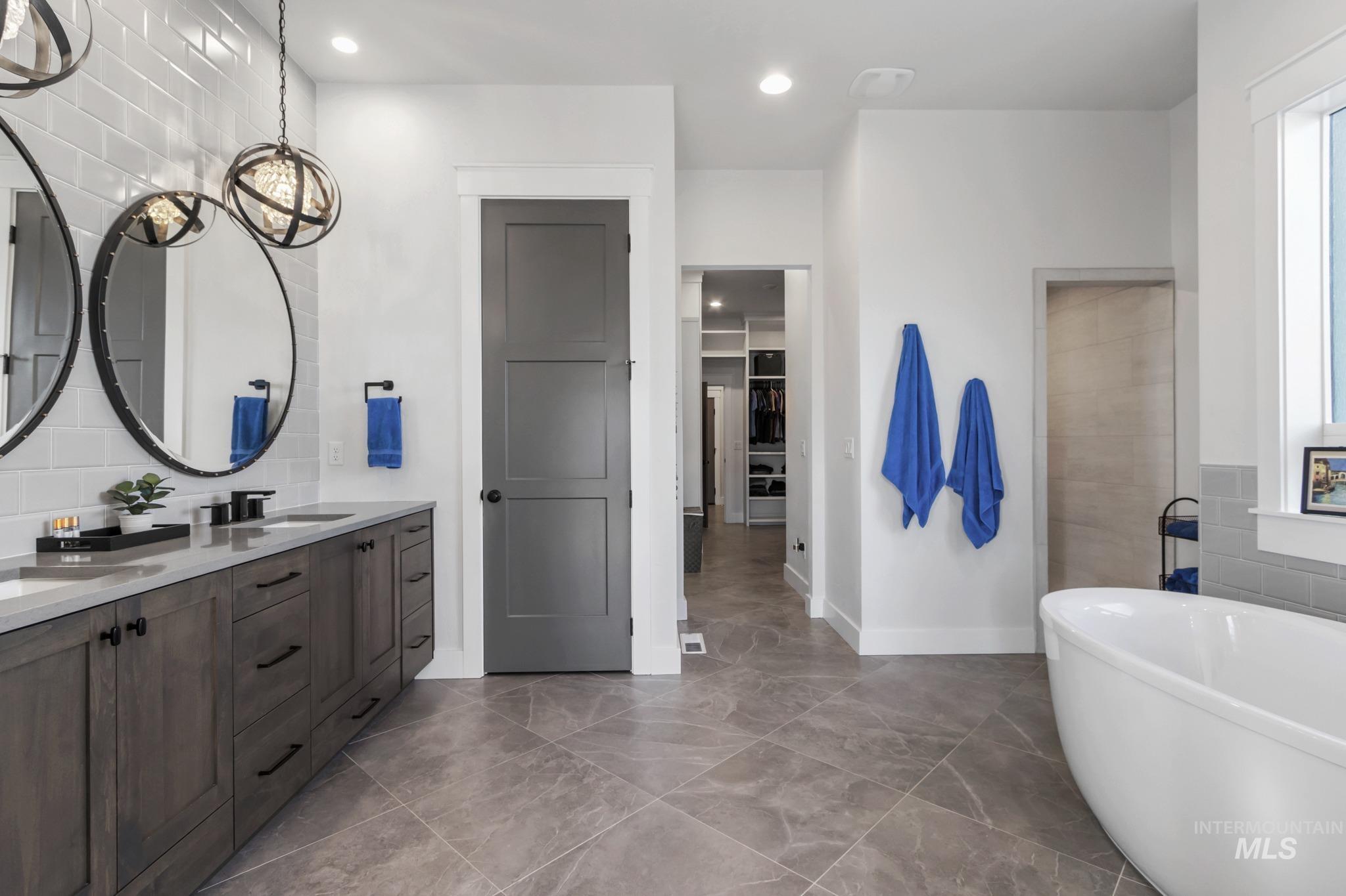 Bathroom featuring a freestanding tub, double vanity, recessed lighting, a walk in closet, and backsplash