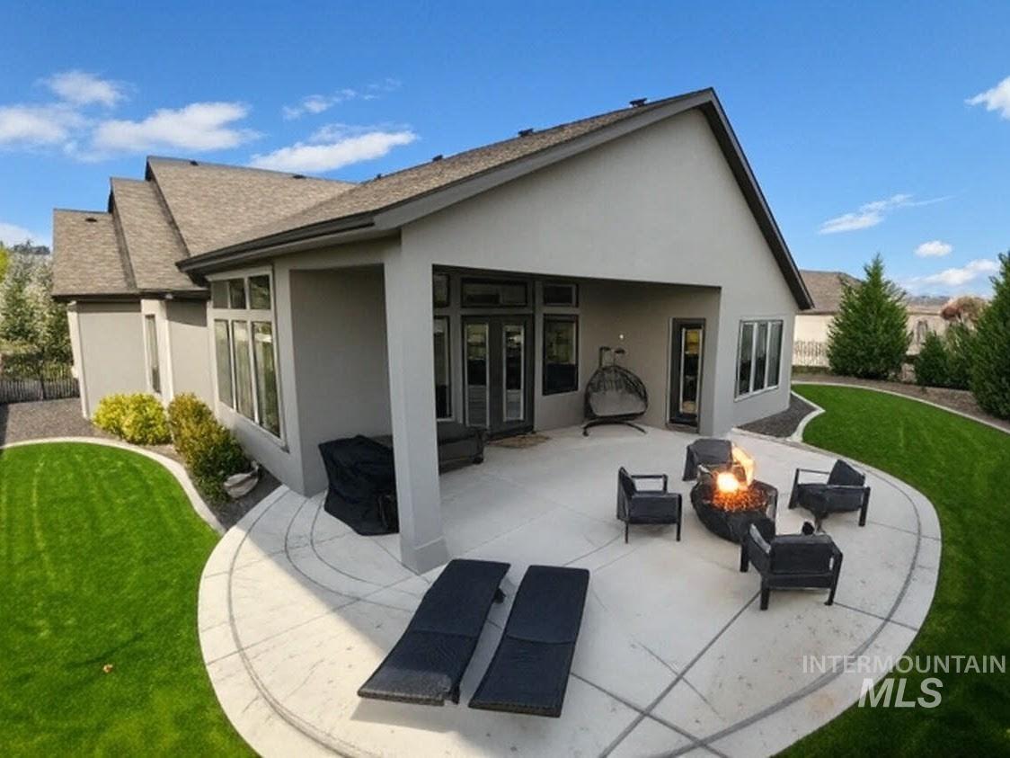 Rear view of property featuring a lawn, a patio, a shingled roof, and an outdoor fire pit