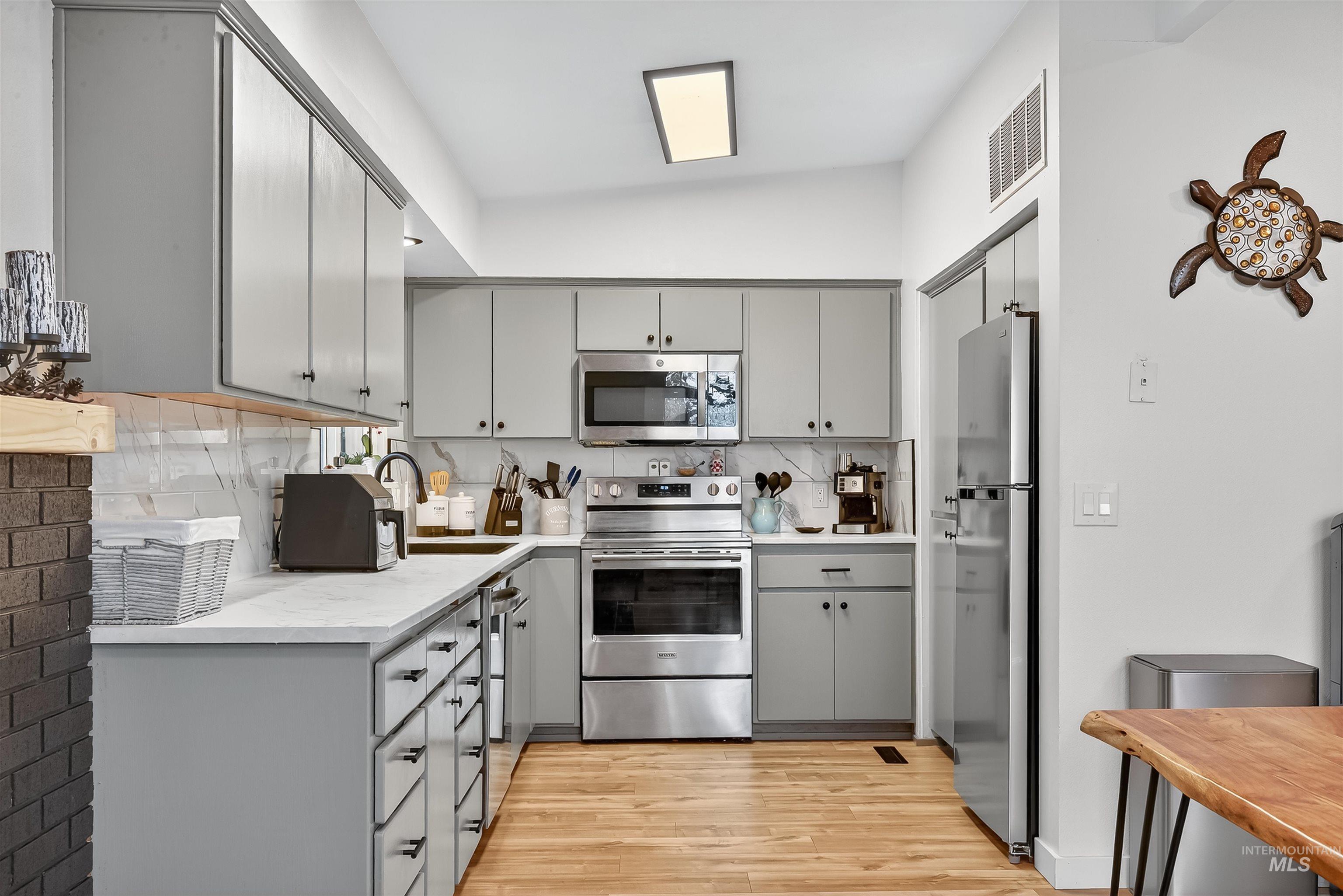 Kitchen with gray cabinetry, stainless steel appliances, light countertops, and backsplash
