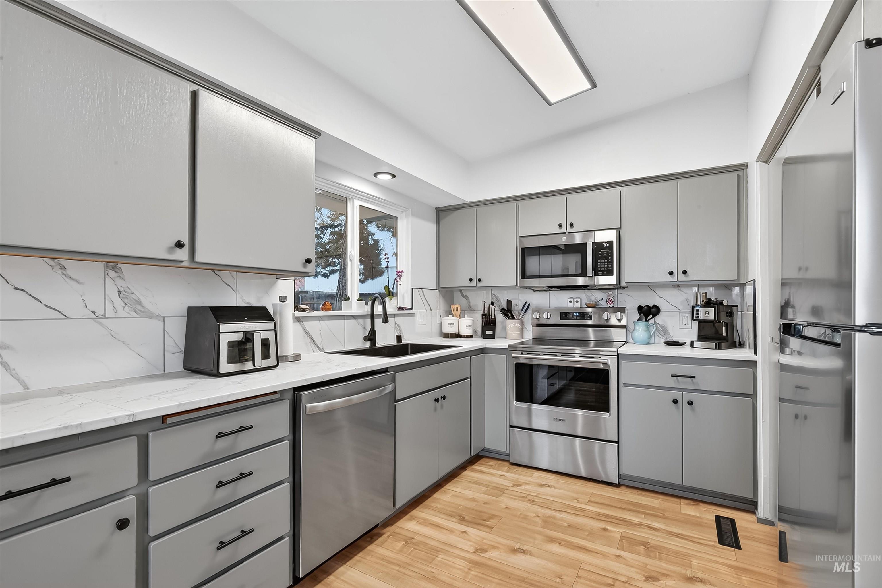 Kitchen with gray cabinets, stainless steel appliances, light wood-type flooring, and decorative backsplash