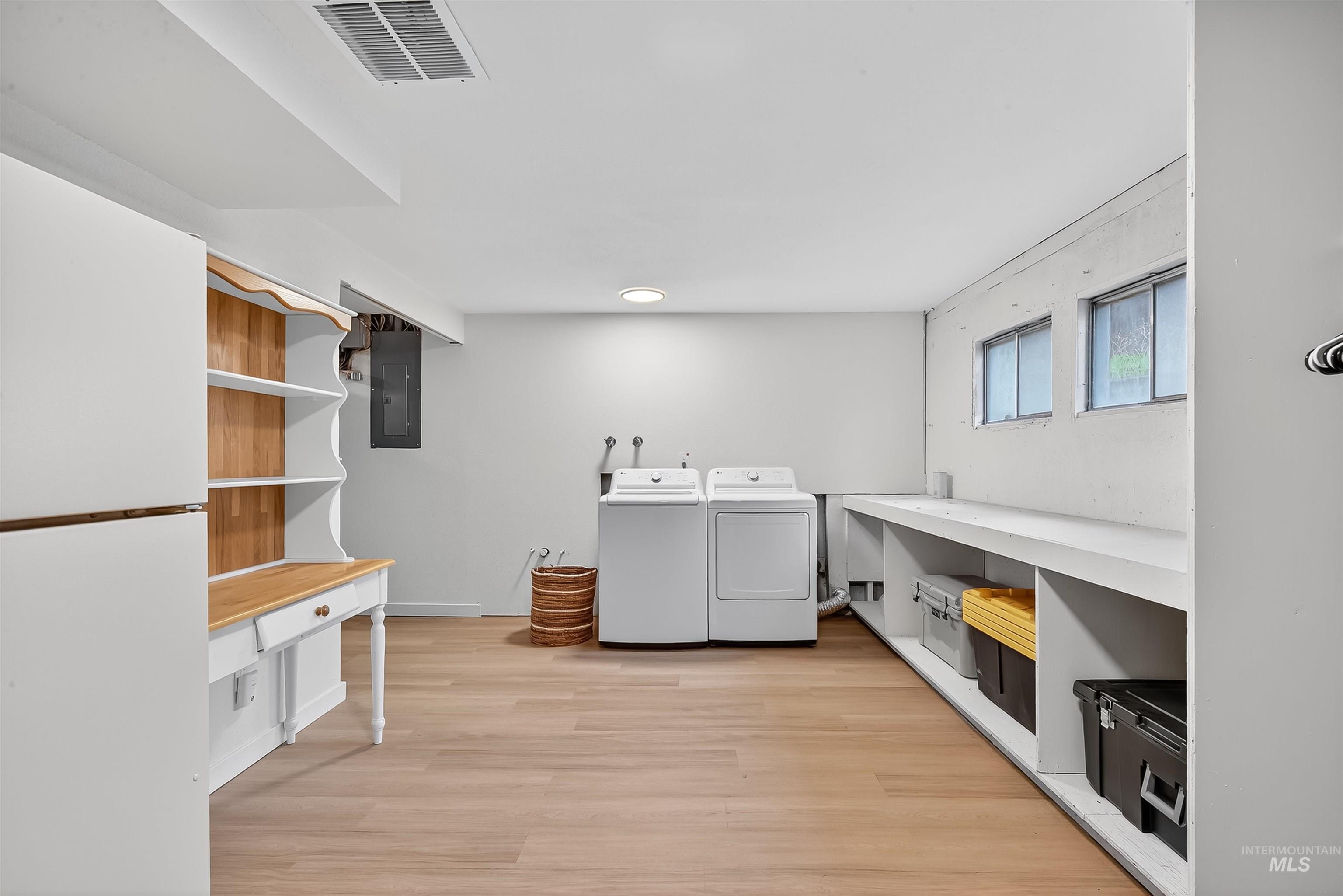 Laundry area with light wood-style flooring, washer and clothes dryer, and electric panel
