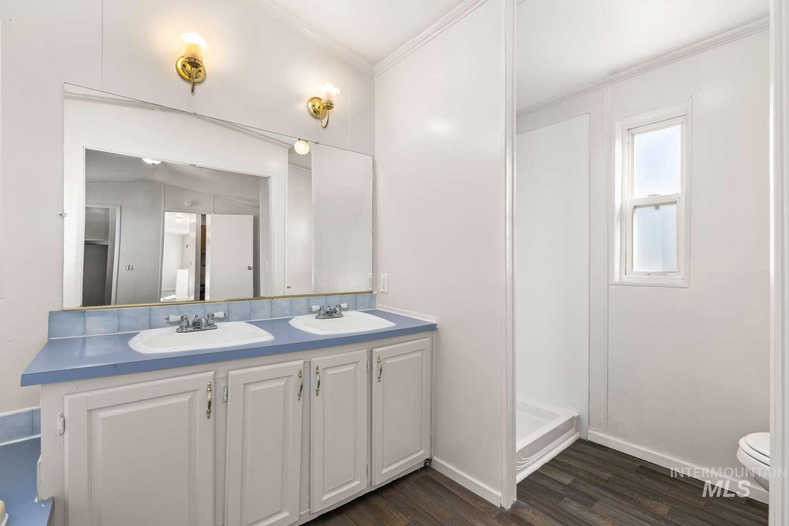 Bathroom featuring double vanity, dark wood-style flooring, ornamental molding, and a shower stall
