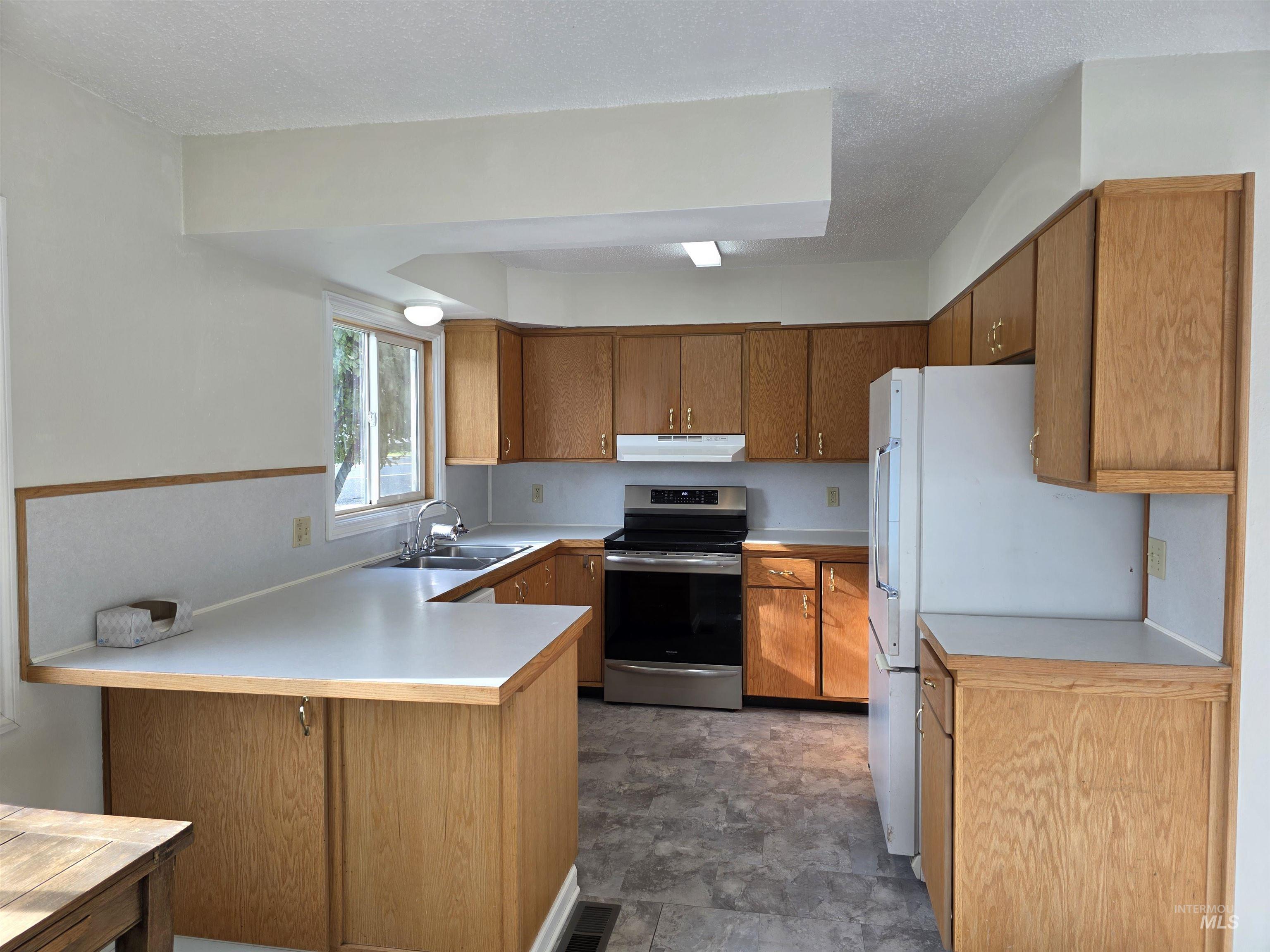 Kitchen with stainless steel range with electric stovetop, brown cabinets, light countertops, freestanding refrigerator, and a peninsula