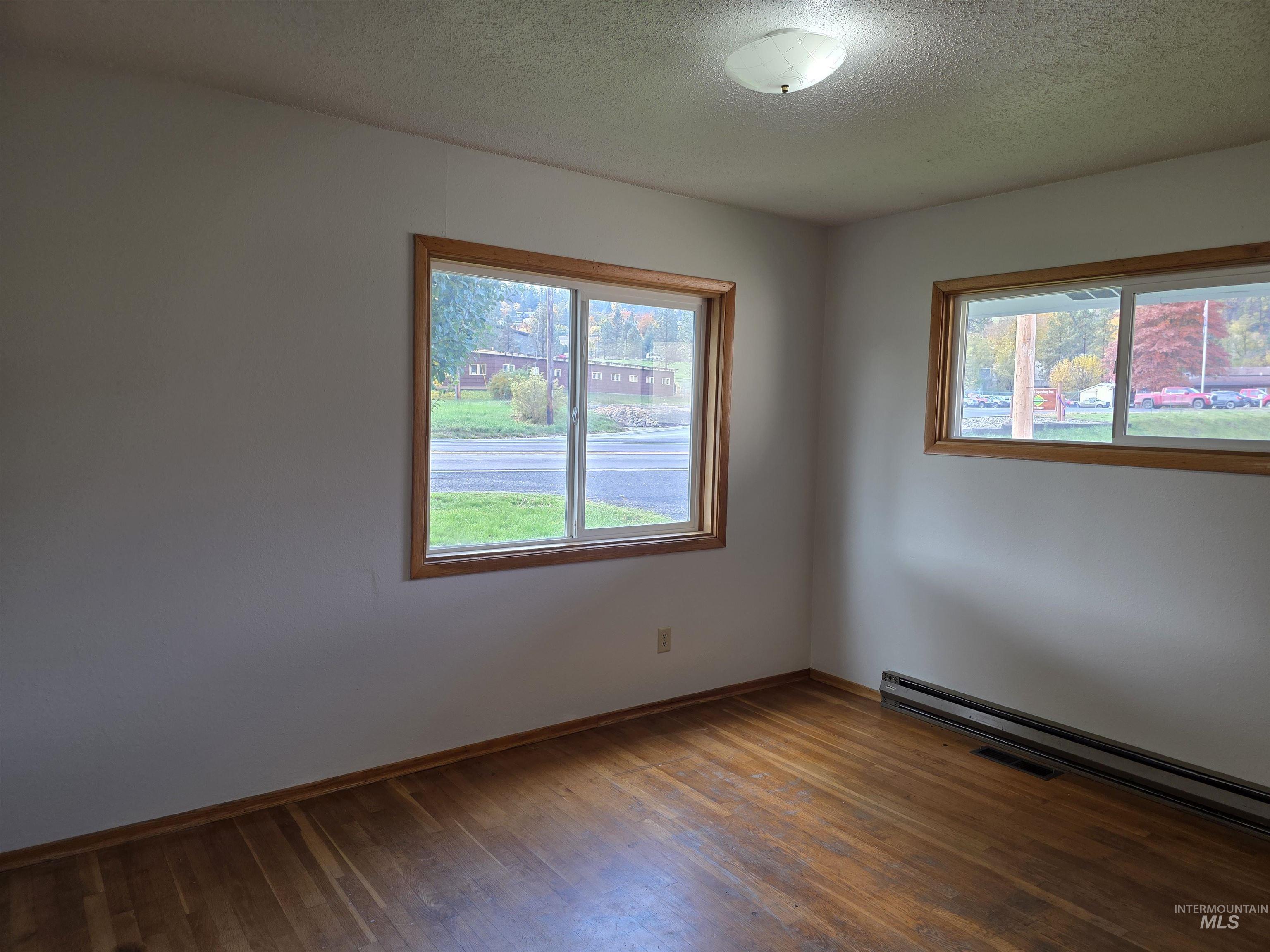 Empty room with a textured ceiling, a baseboard heating unit, and wood finished floors
