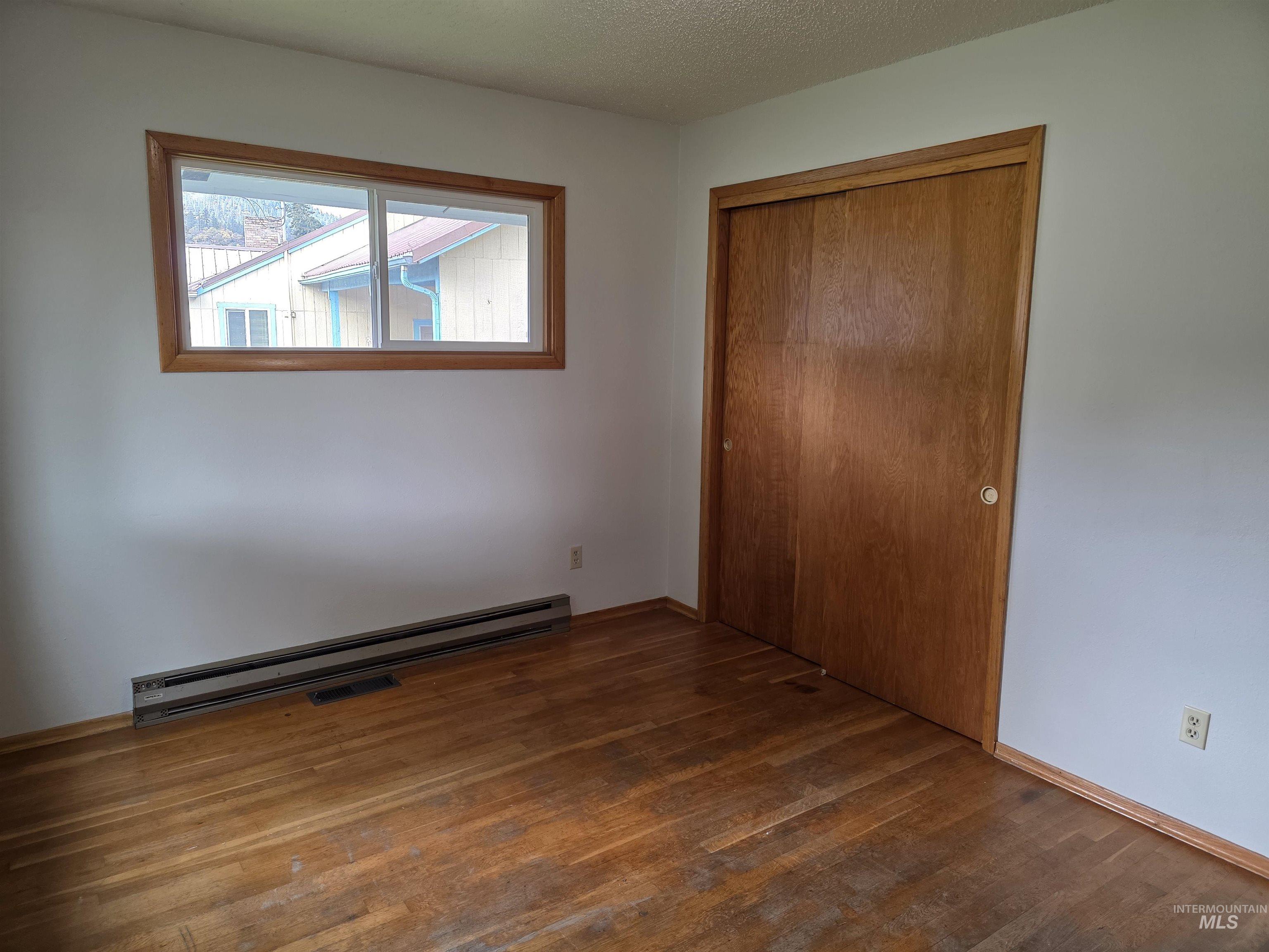 Unfurnished bedroom featuring a baseboard heating unit, dark wood-style flooring, a textured ceiling, and a closet