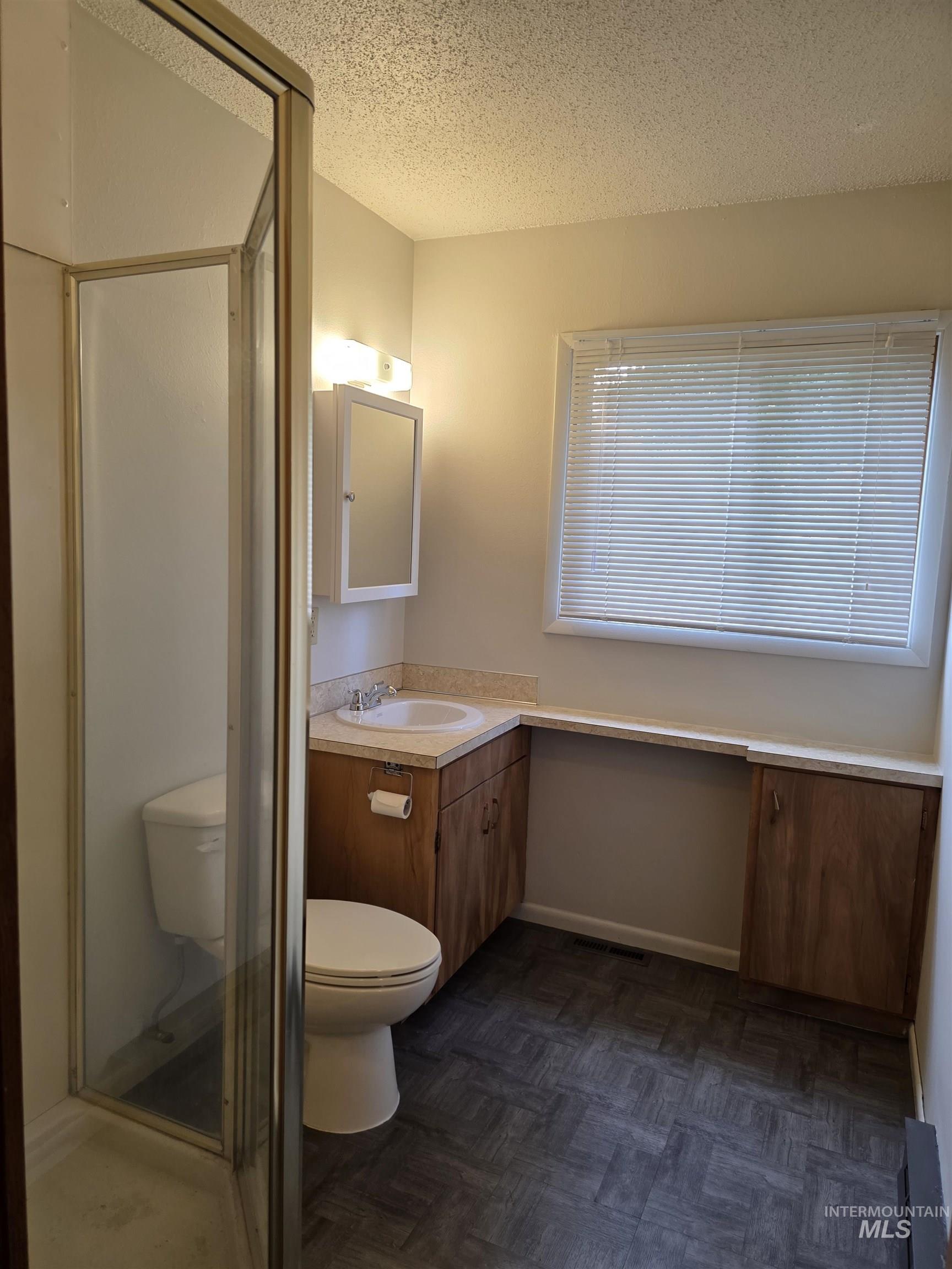 Bathroom featuring vanity, a textured ceiling, a stall shower, and a baseboard radiator