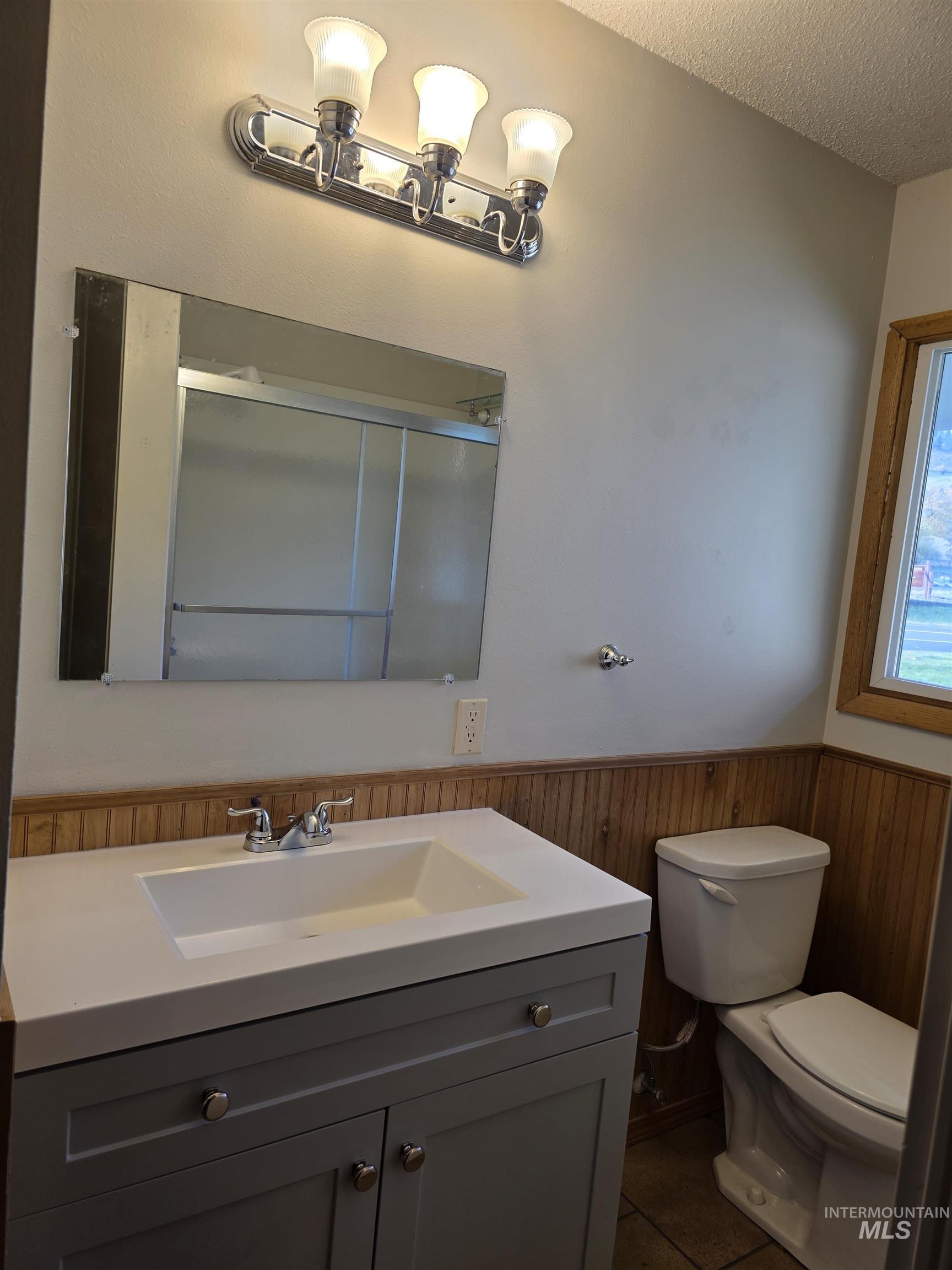 Bathroom featuring vanity, a stall shower, a textured ceiling, dark tile patterned flooring, and a wainscoted wall