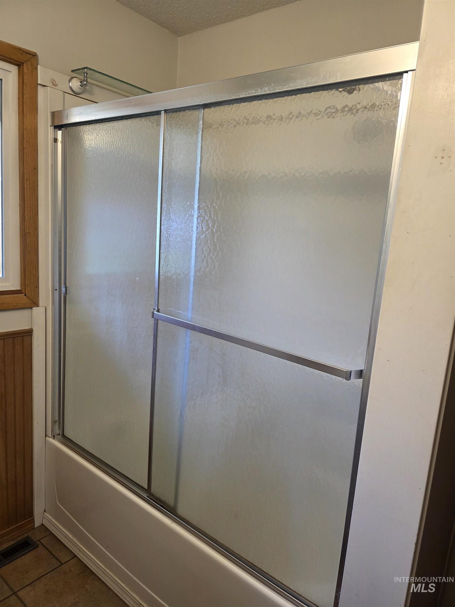 Full bathroom featuring shower / bath combination with glass door, tile patterned floors, and a textured ceiling