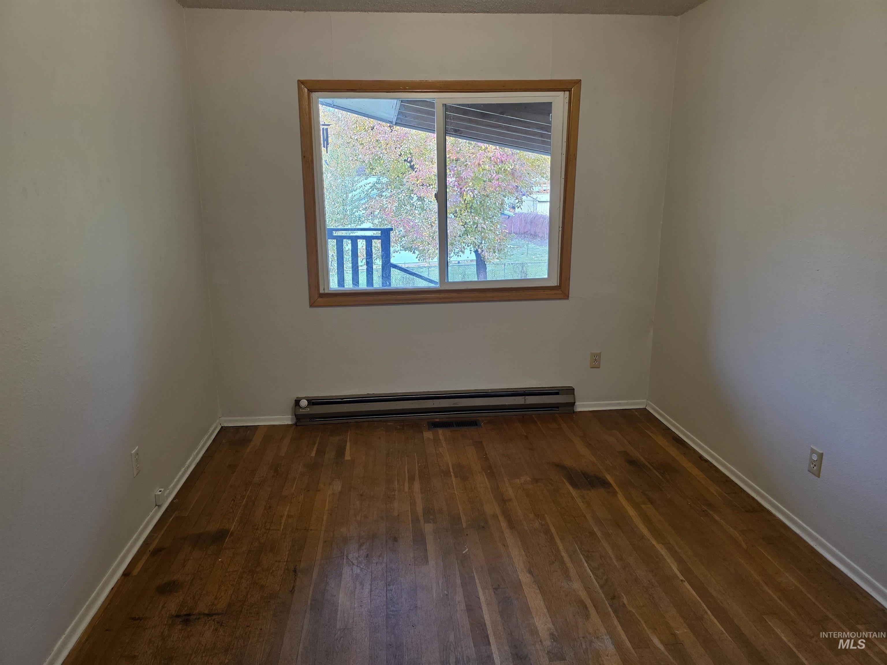 Unfurnished room featuring dark wood-type flooring and a baseboard heating unit