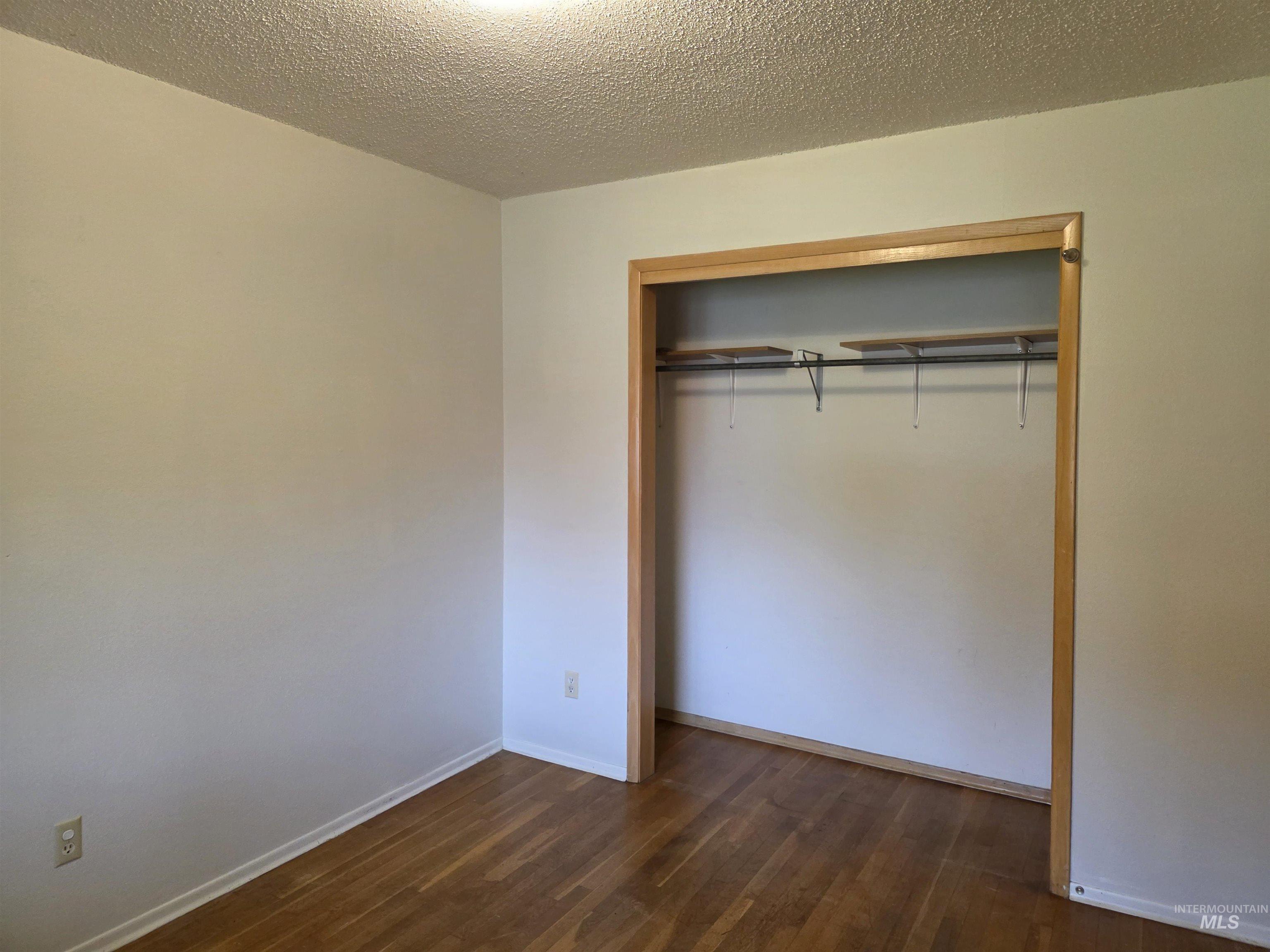 Unfurnished bedroom featuring a textured ceiling, dark wood-type flooring, and a closet