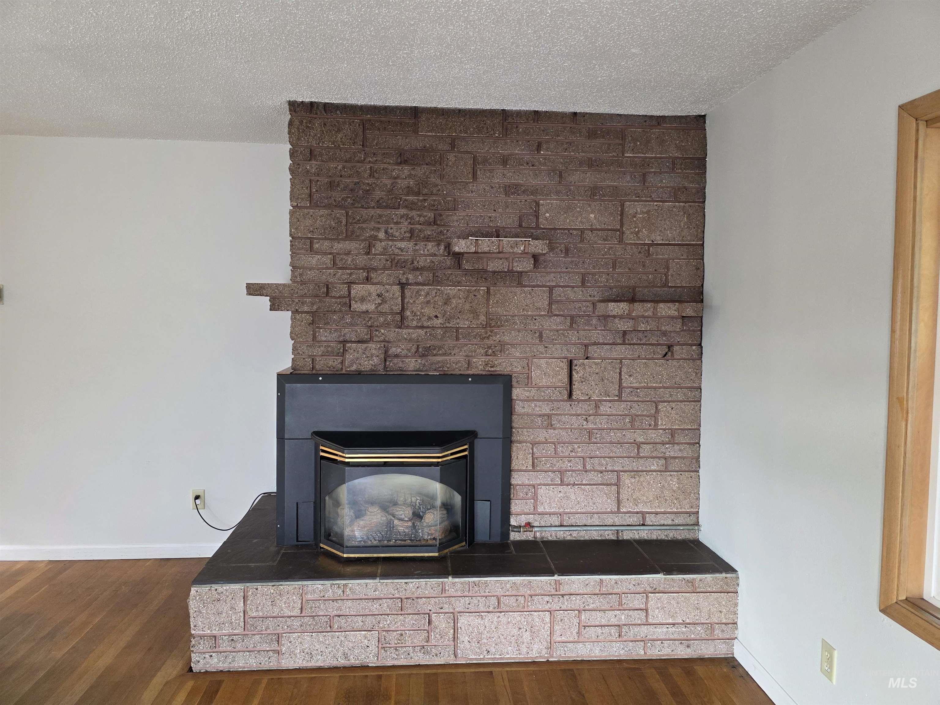 Detailed view of a textured ceiling, wood finished floors, and a large fireplace