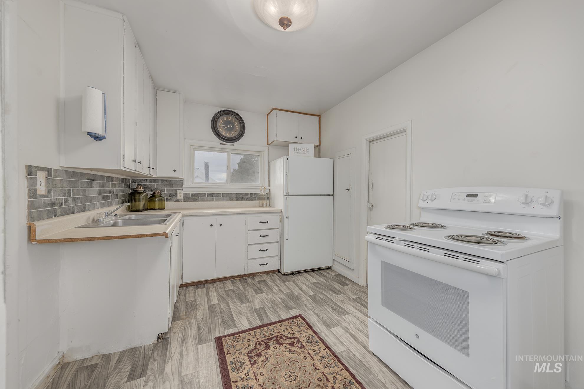Kitchen with white appliances, white cabinets, light countertops, and decorative backsplash