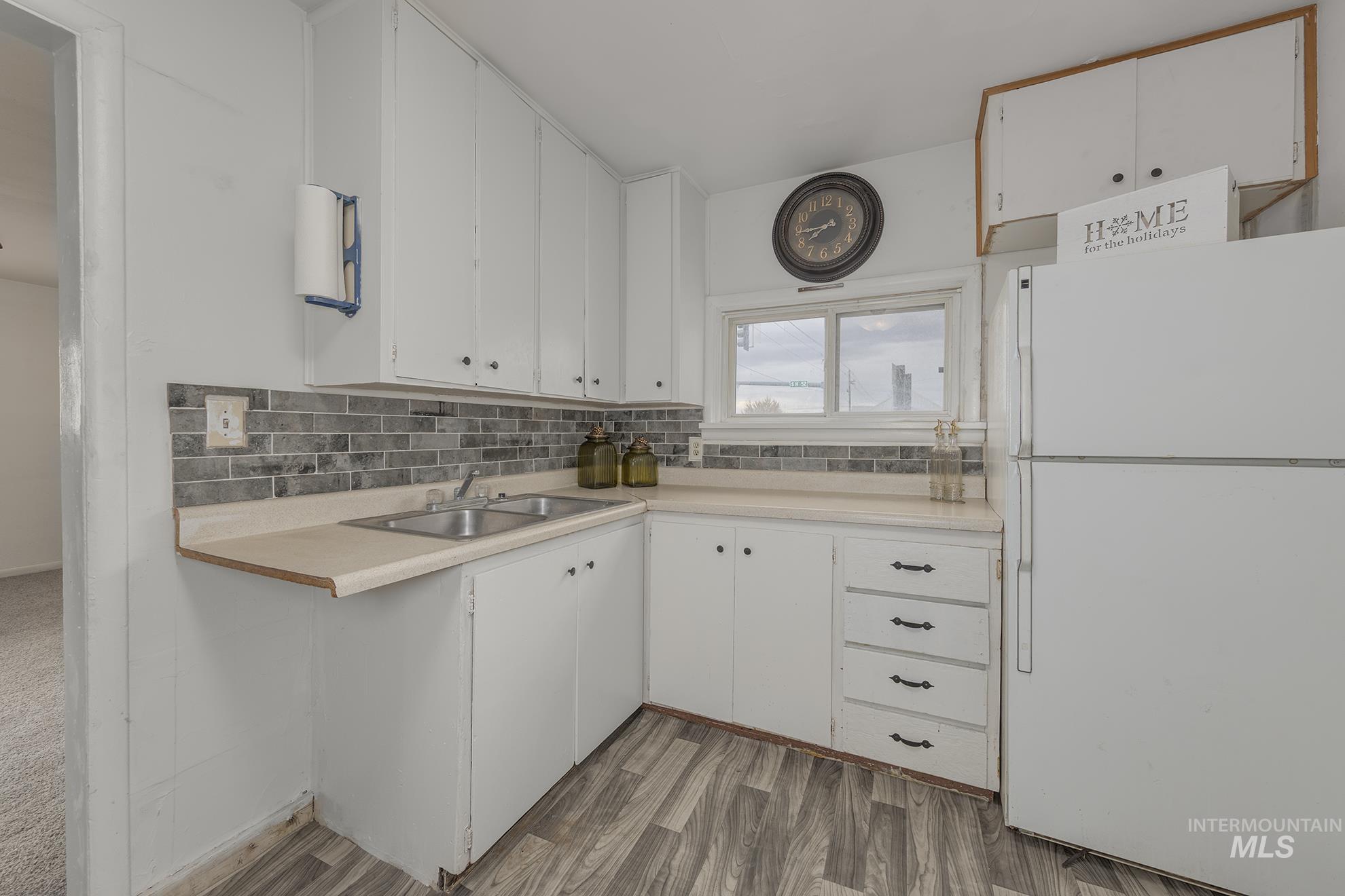 Kitchen featuring white cabinetry, freestanding refrigerator, light countertops, tasteful backsplash, and light wood-type flooring