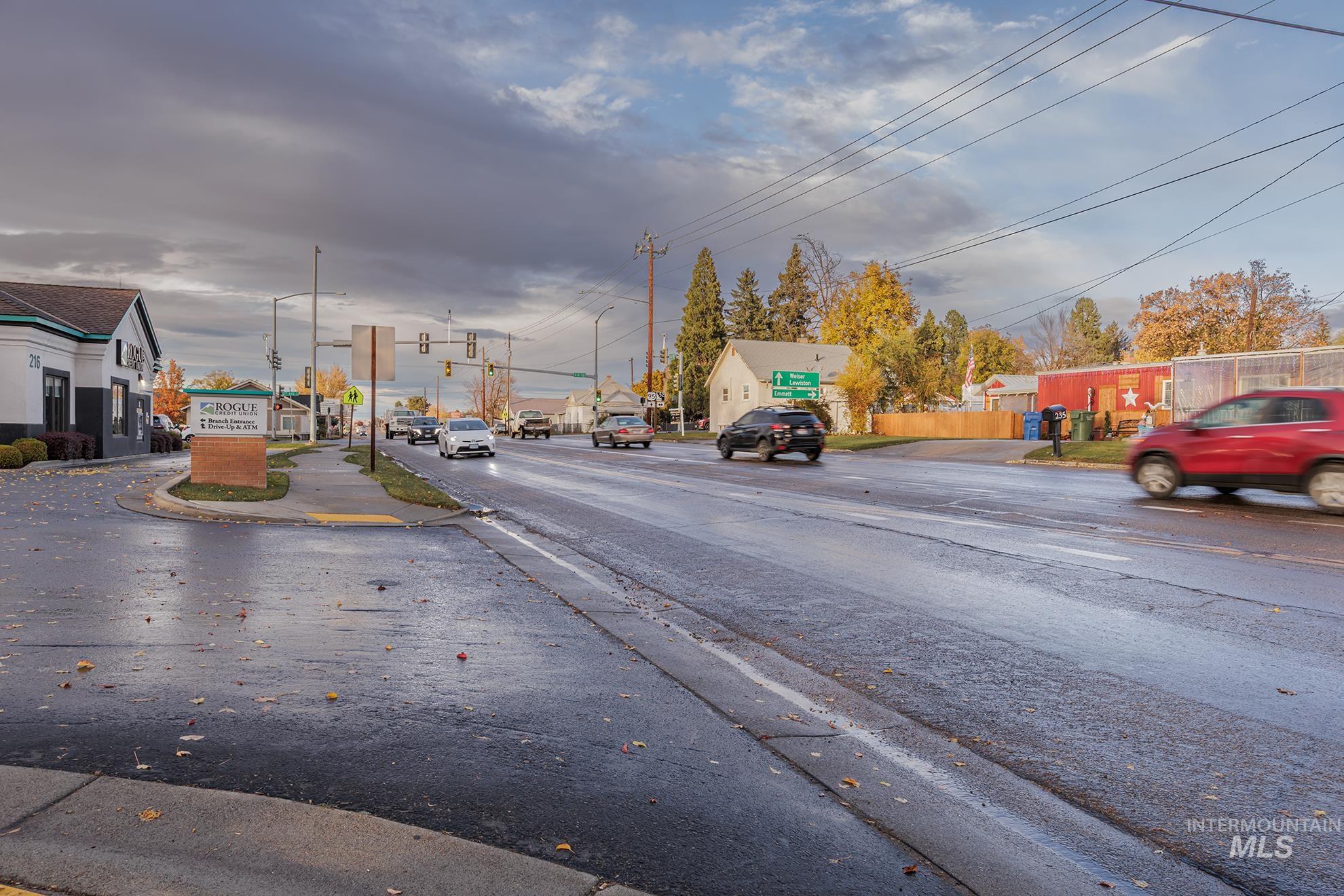 View of asphalt road featuring traffic lights, curbs, and sidewalks