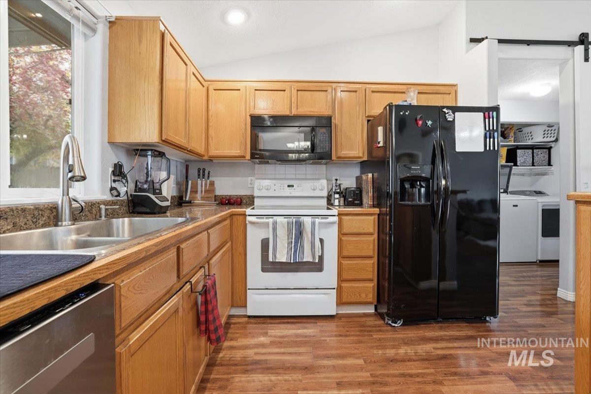 Kitchen featuring black appliances, dark wood-style floors, a barn door, lofted ceiling, and backsplash