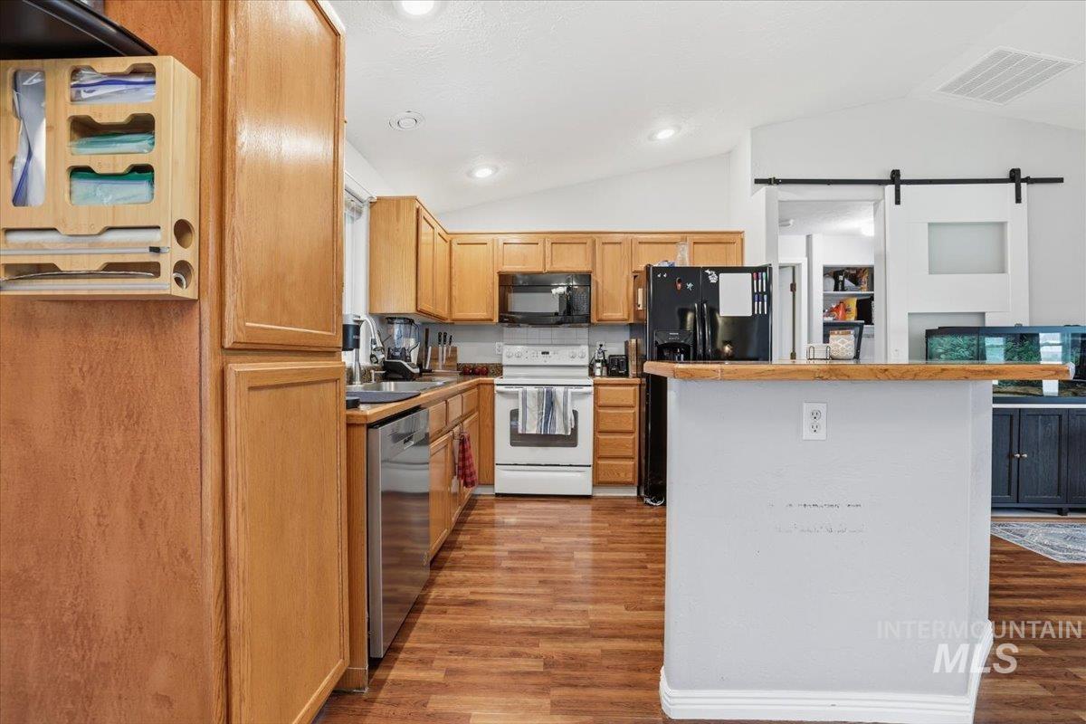 Kitchen with a barn door, lofted ceiling, black appliances, light wood finished floors, and a center island