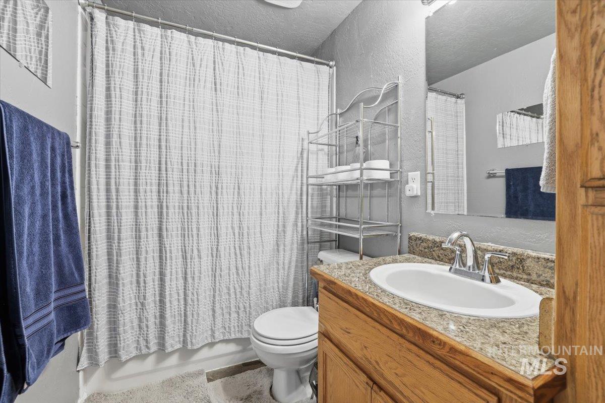Bathroom featuring a textured wall, vanity, shower / bathtub combination with curtain, and a textured ceiling