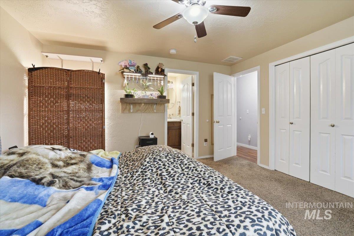 Bedroom featuring light colored carpet, a textured ceiling, a ceiling fan, a closet, and ensuite bath