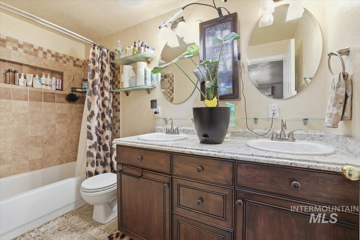 Full bath with shower / tub combo with curtain, double vanity, and a textured ceiling