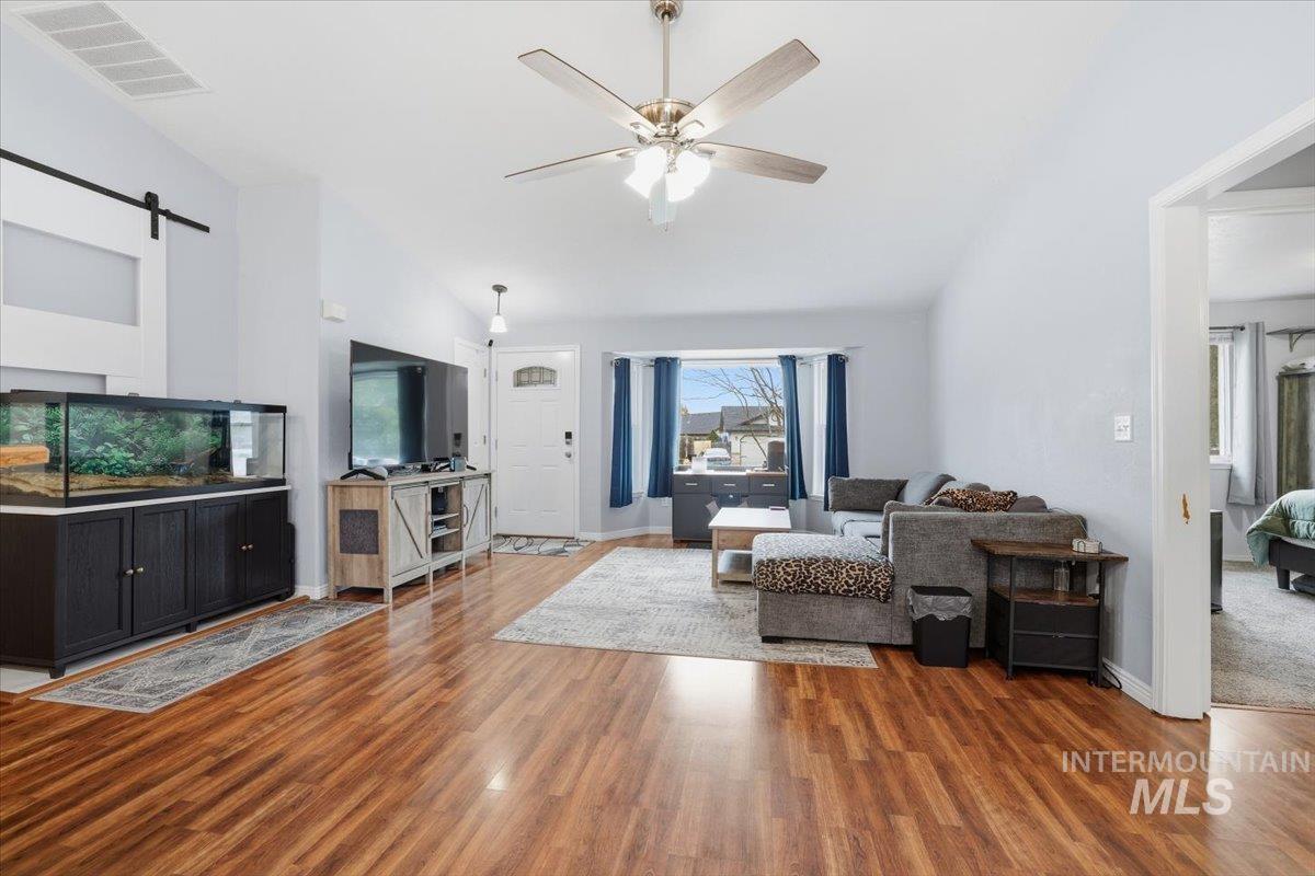 Living area featuring a barn door, ceiling fan, light wood finished floors, and vaulted ceiling