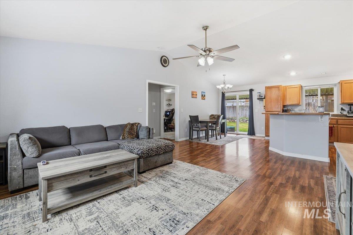 Living area featuring dark wood-type flooring, vaulted ceiling, a ceiling fan, a chandelier, and recessed lighting