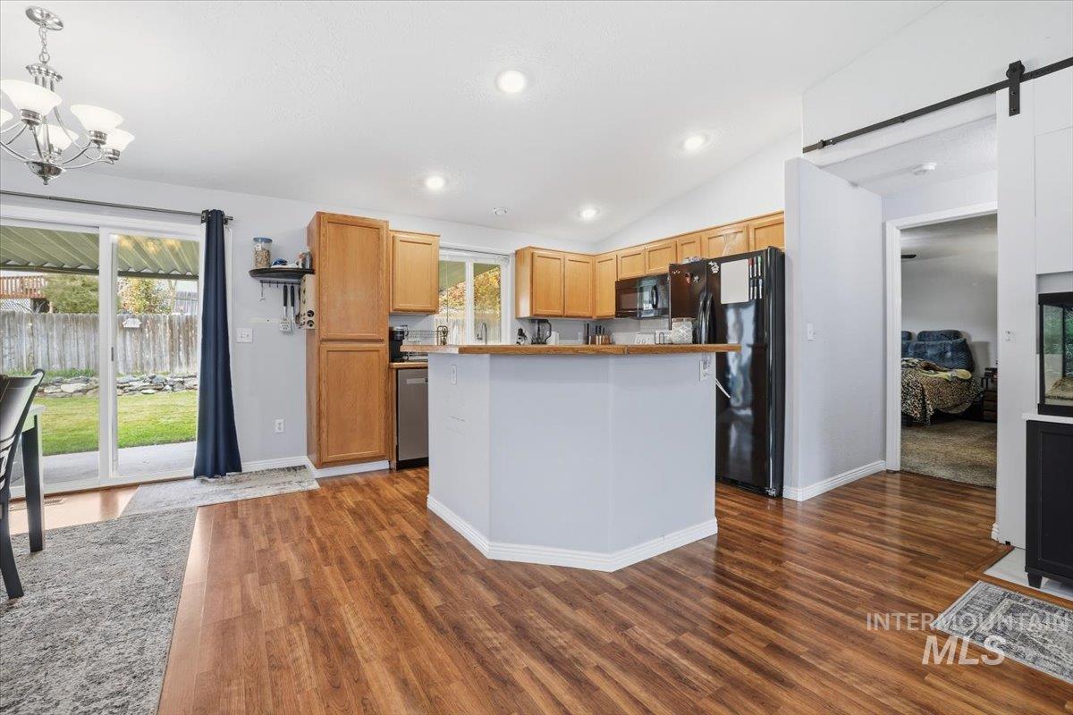 Kitchen featuring a barn door, vaulted ceiling, black appliances, dark wood-style flooring, and pendant lighting