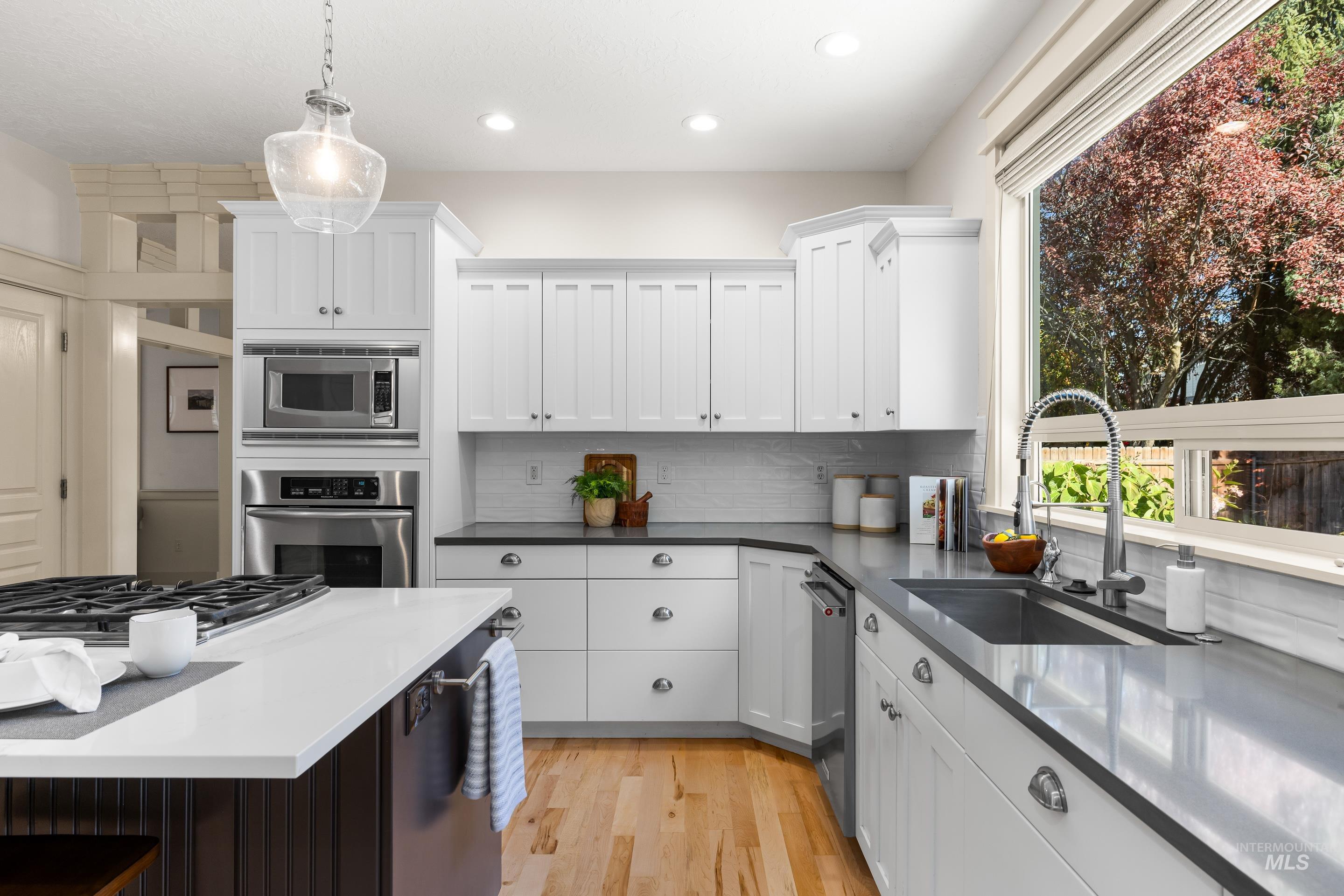 Kitchen with appliances with stainless steel finishes, decorative light fixtures, light wood-style flooring, white cabinets, and dark stone counters