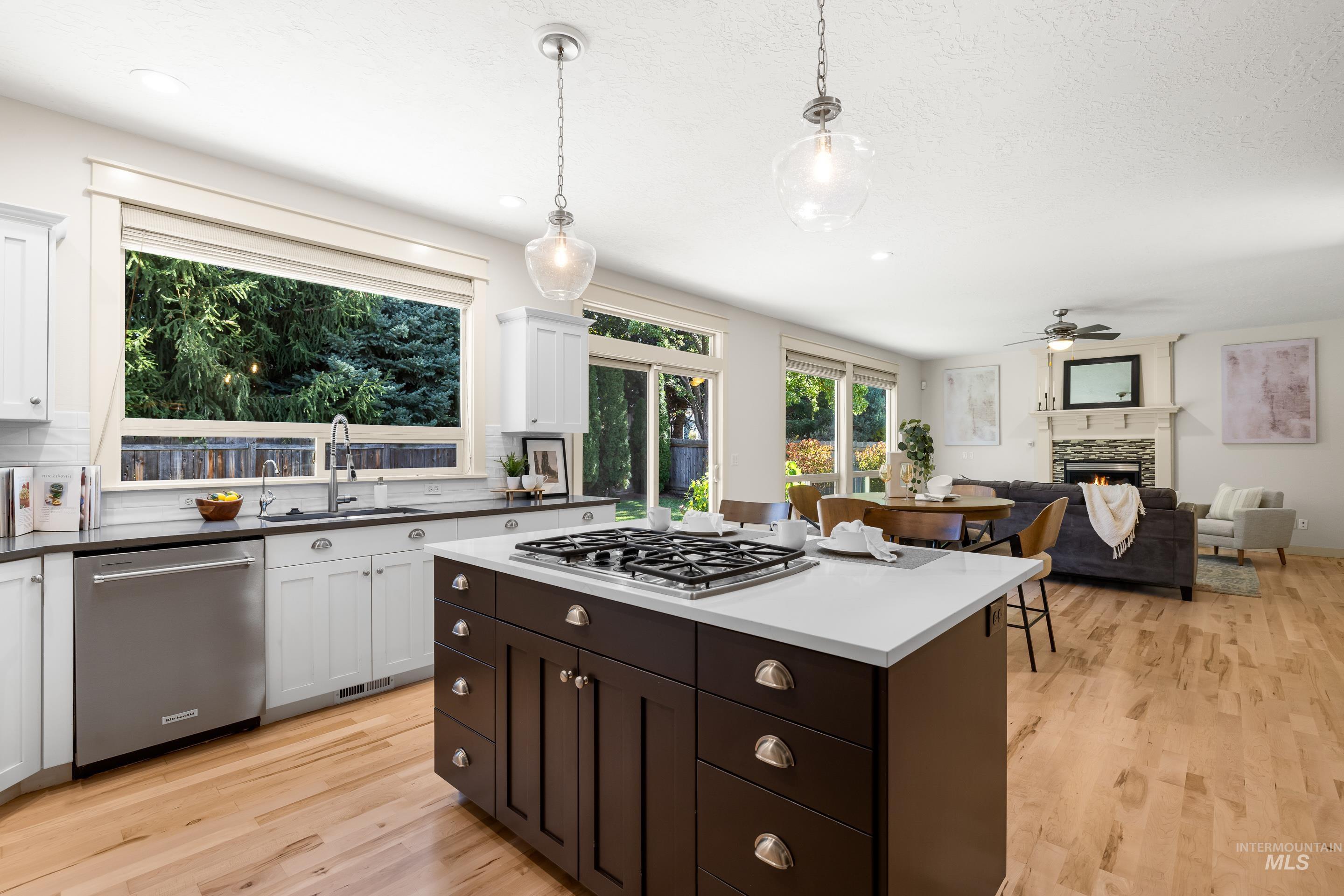 Kitchen with a lit fireplace, pendant lighting, appliances with stainless steel finishes, and light wood-type flooring